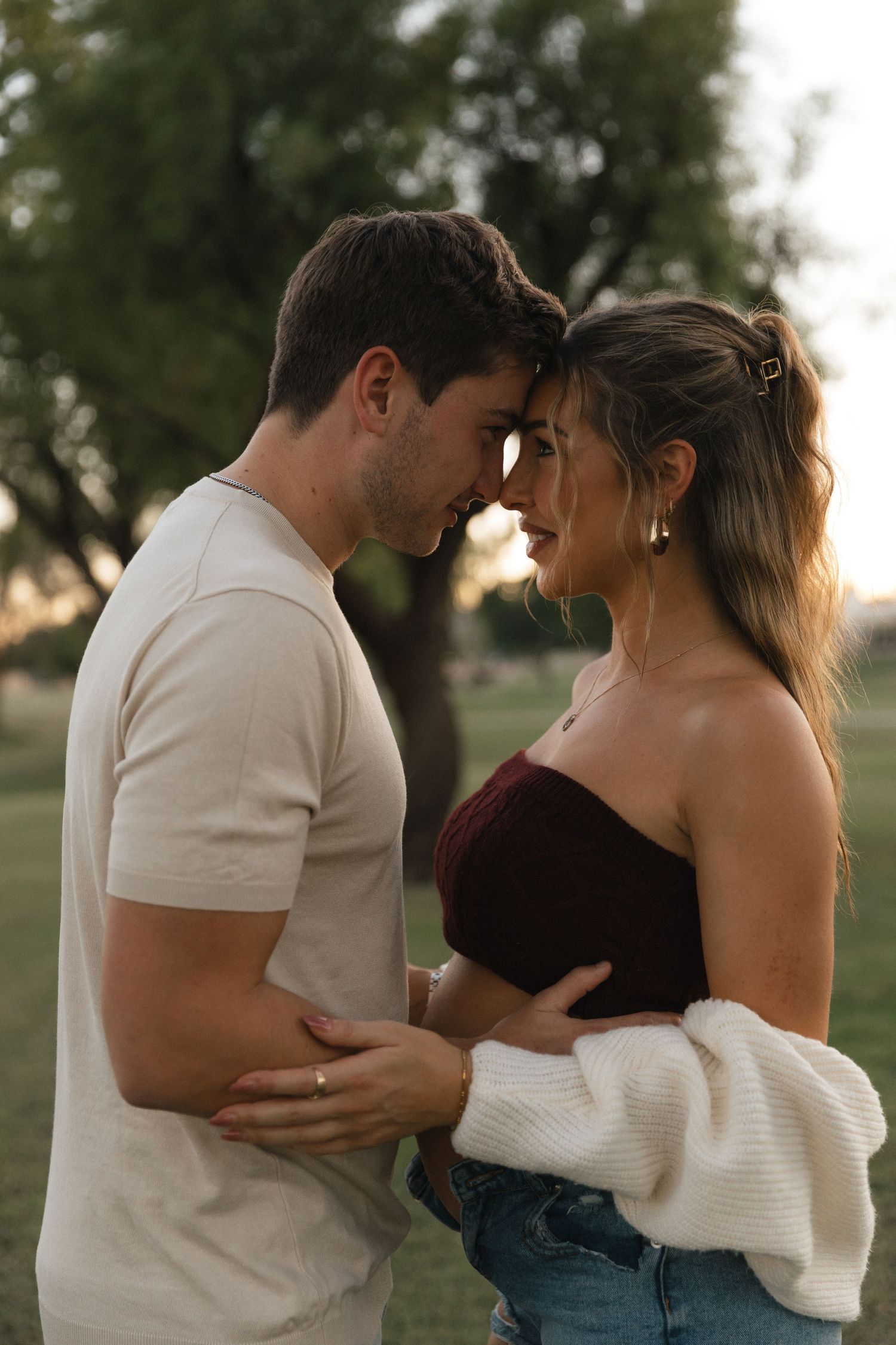 Romantic couples embrace in an outdoor setting at sunset wearing casual white and dark clothing.