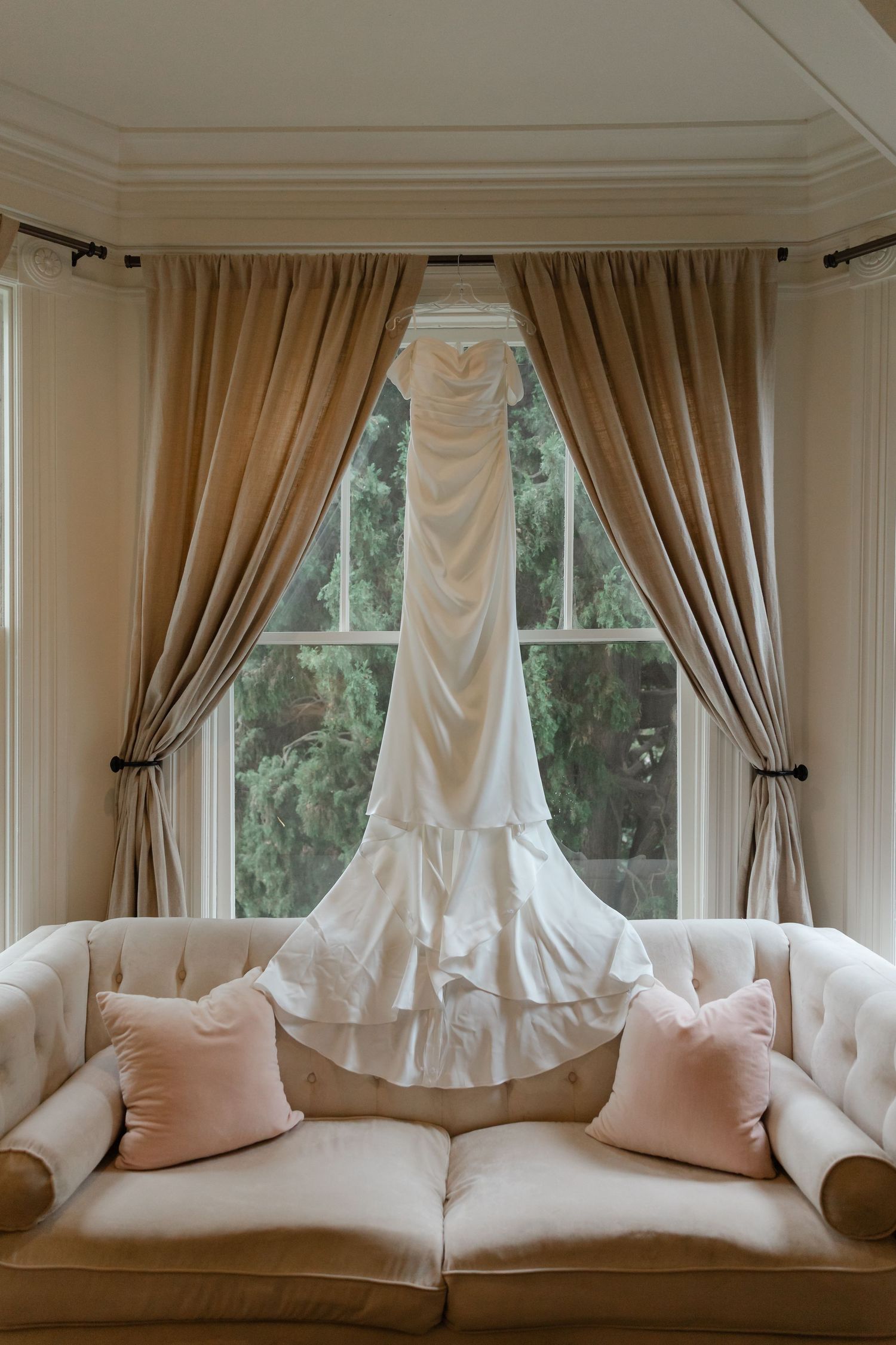 Elegant bay window with cream-colored curtains and plush white cushioned seating creates a cozy reading nook.