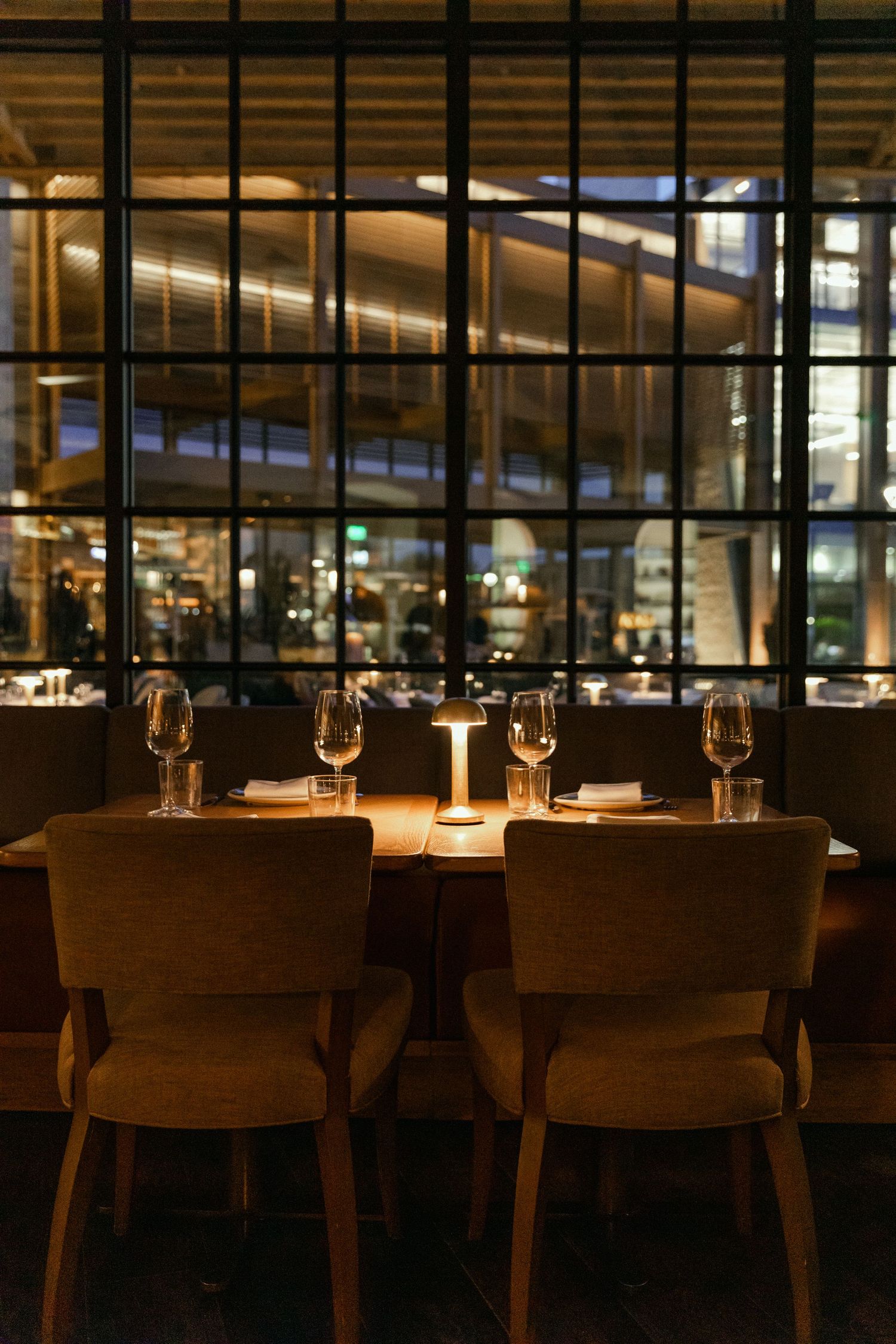 Intimate restaurant table setting with candlelight against large windows showcasing modern architecture.