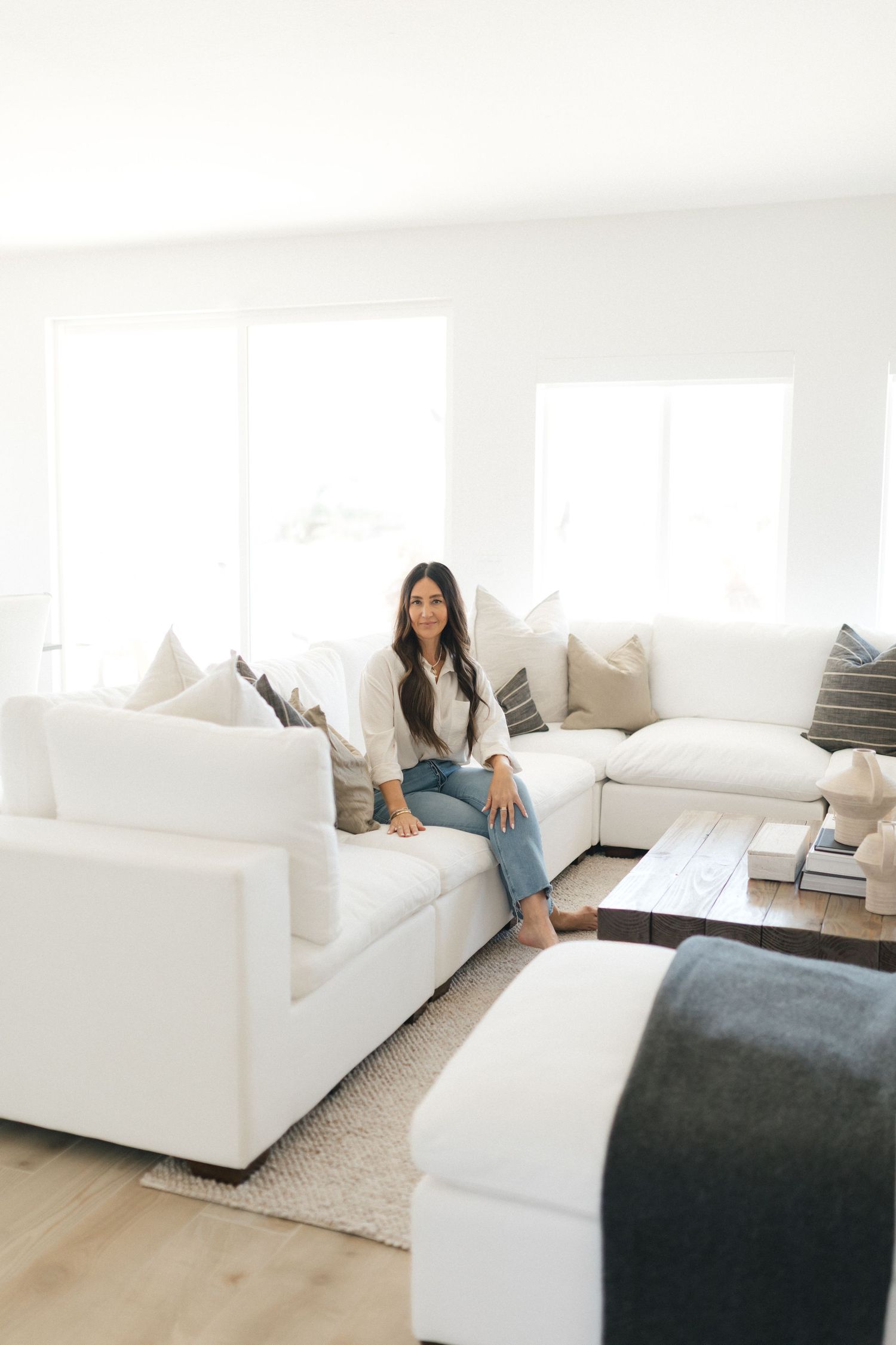 Minimalist living room with white sofa, grey throw blanket, and light hardwood floors showcases modern interior design style.