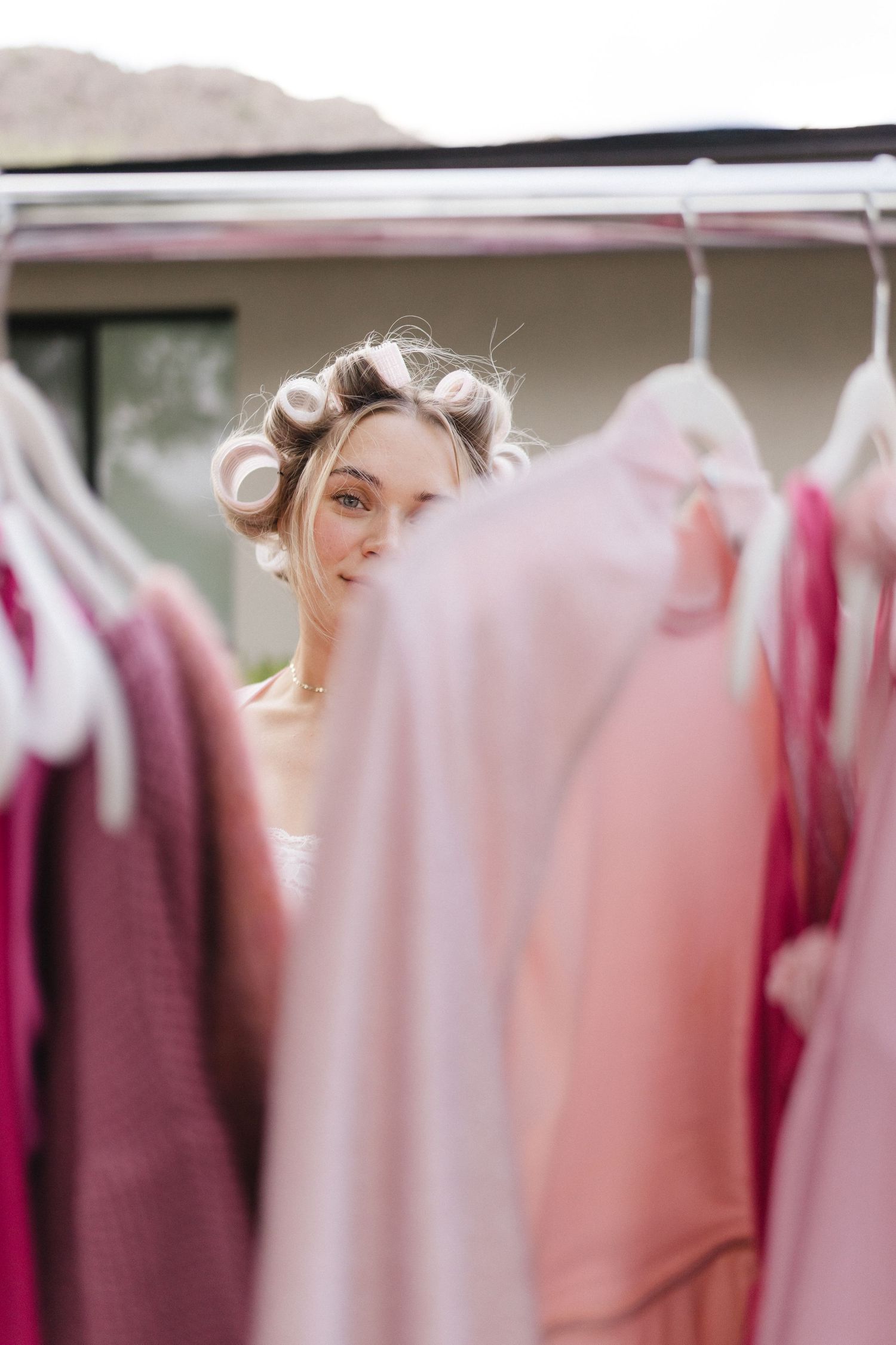 Woman with hair curlers browsing pink clothing on an outdoor rack.