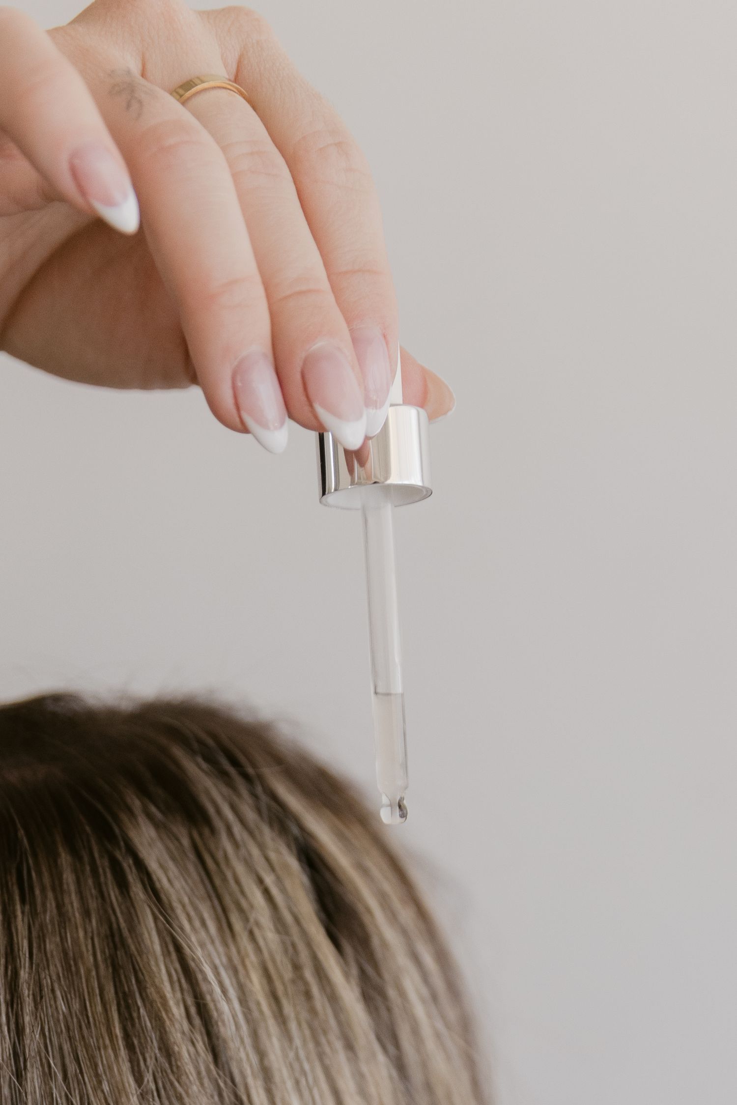 Woman with French manicure holding a dropper pipette with serum above her hair for scalp treatment.