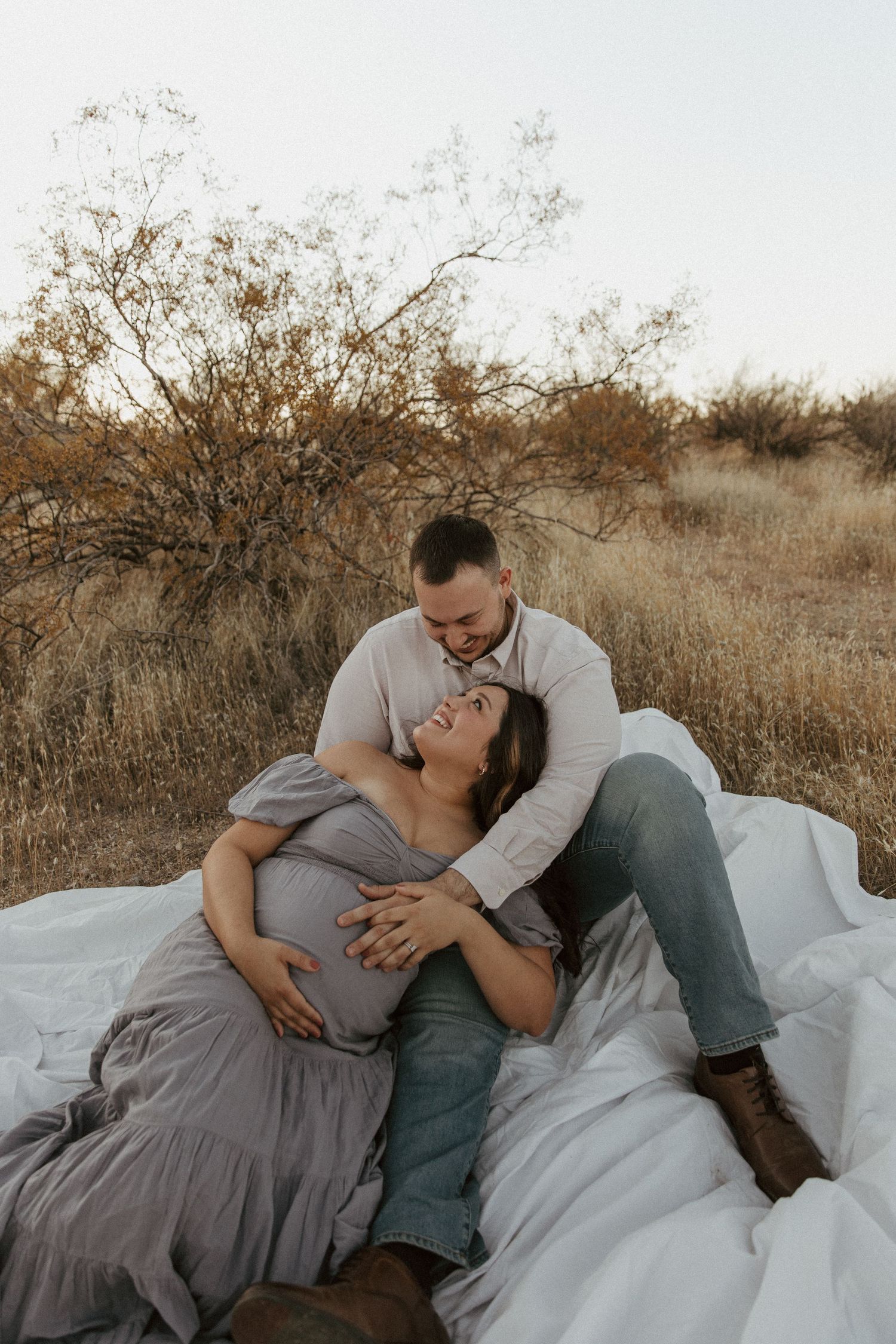 A couple shares an intimate moment while resting on blankets in a desert setting.