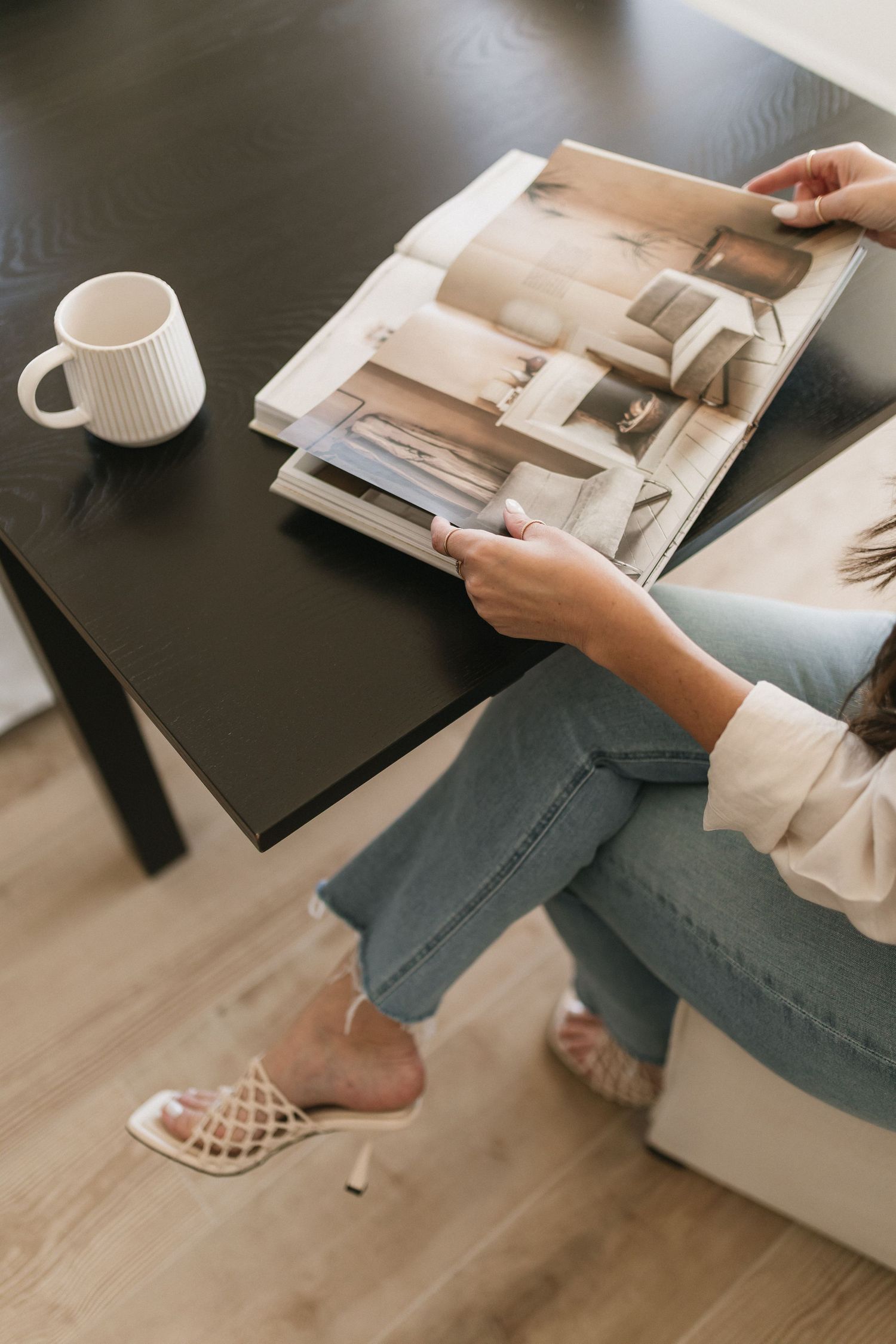 Person relaxing on couch with coffee and magazine in a minimalist living room setting.