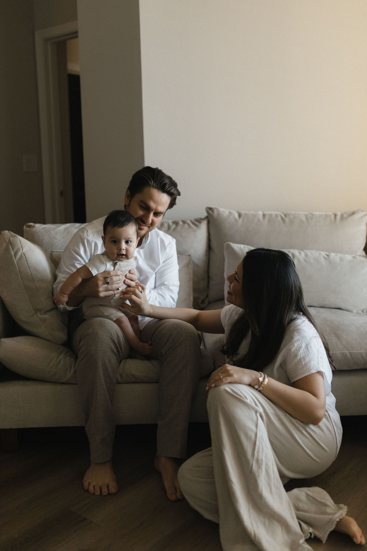 A couple in white clothing sits together on a light-colored couch in a series of intimate poses.
