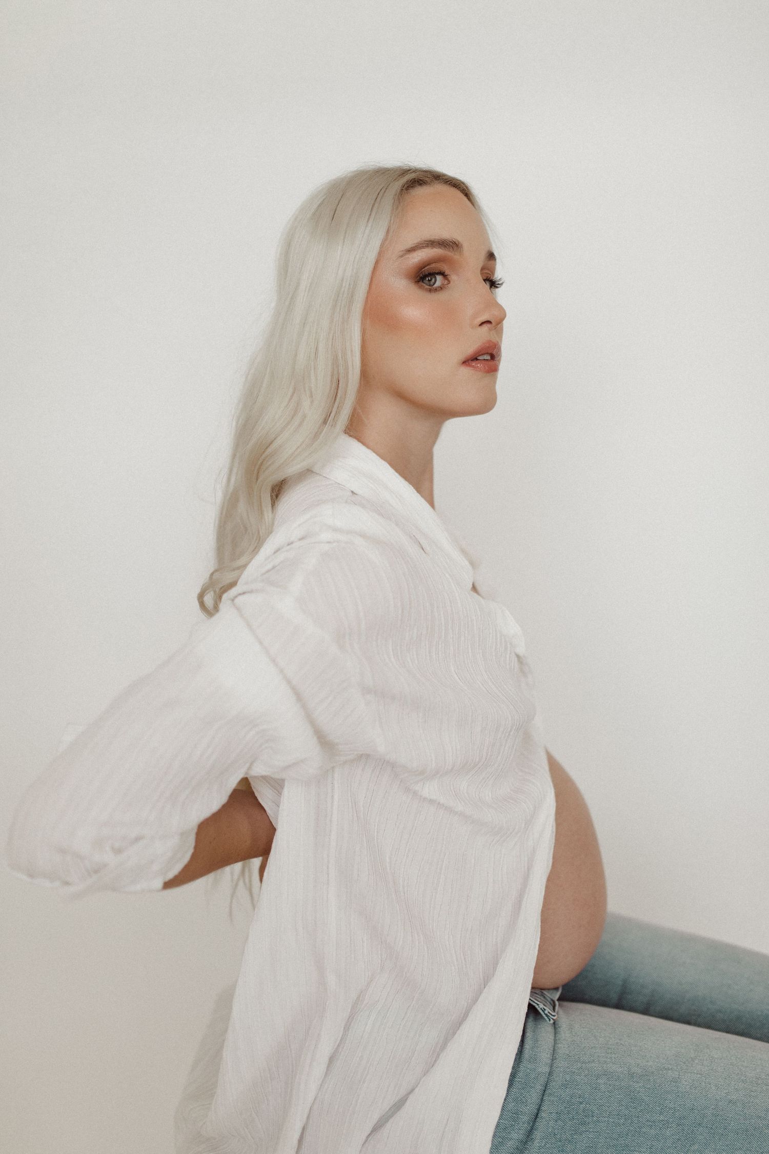 Side profile of pregnant woman in white shirt against neutral background.