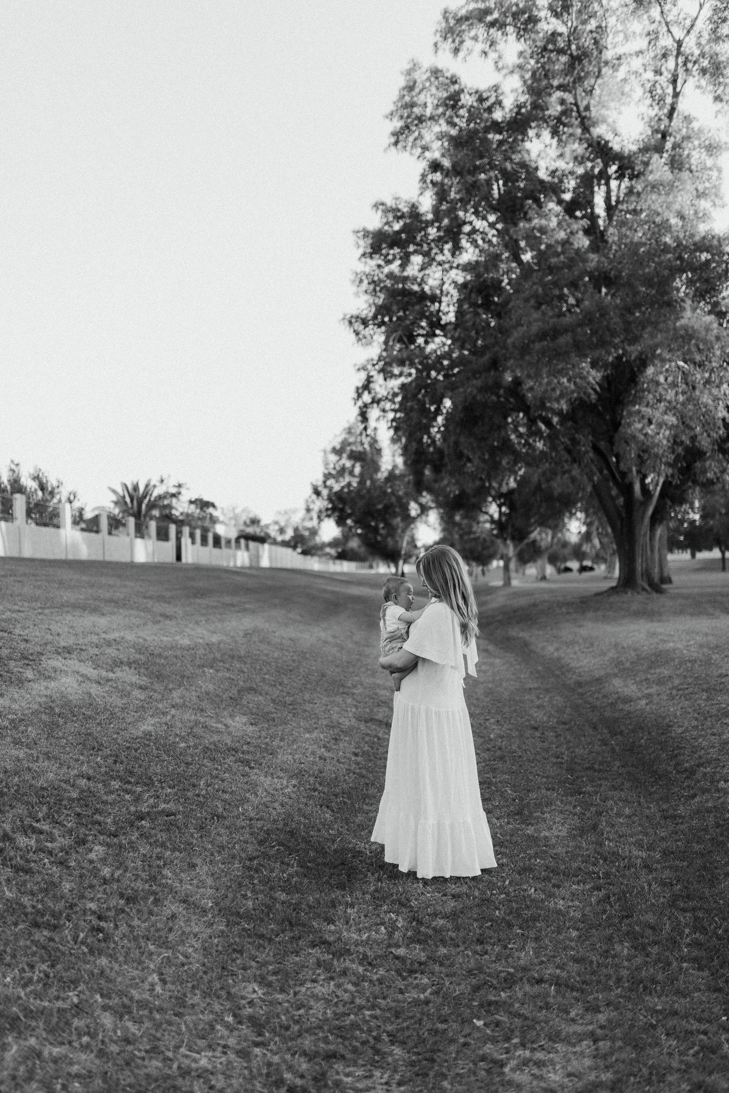 Black and white photo of woman holding baby while standing in park path.