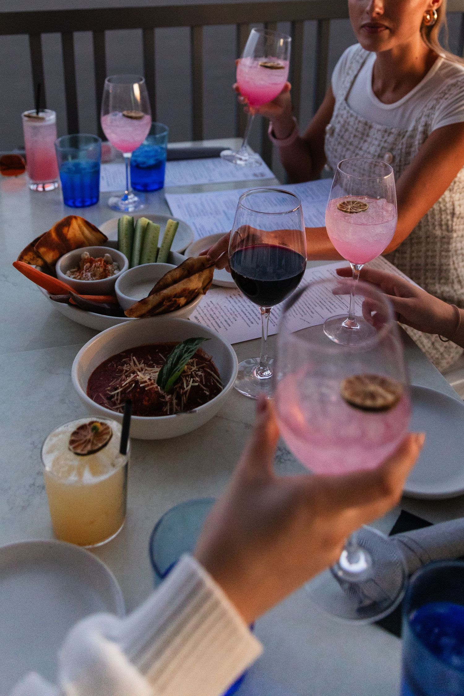 Colorful cocktails and appetizers being served at a dinner gathering with wine glasses.