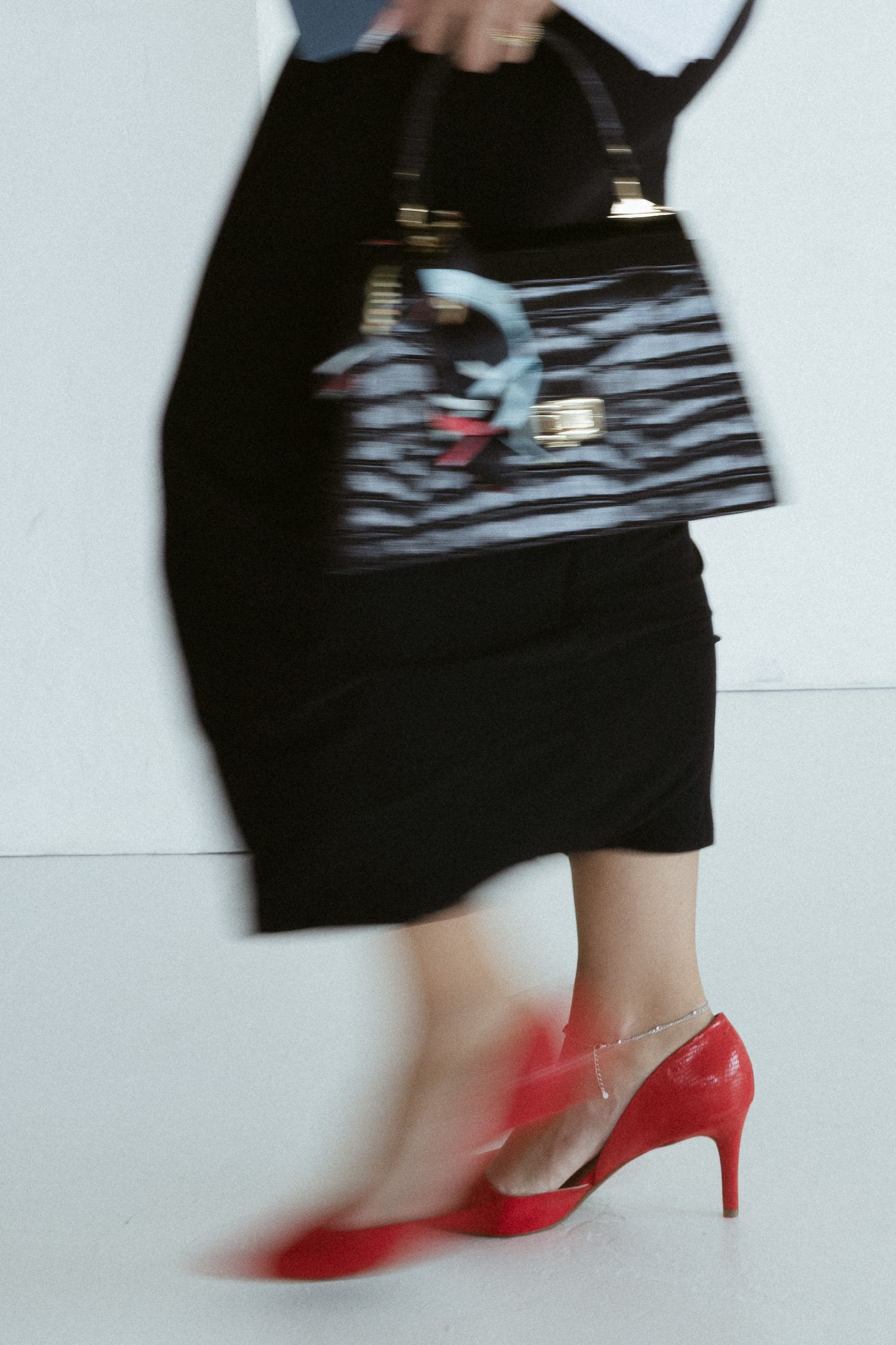 Woman in black skirt and red heels carrying a striped handbag, captured in motion blur.