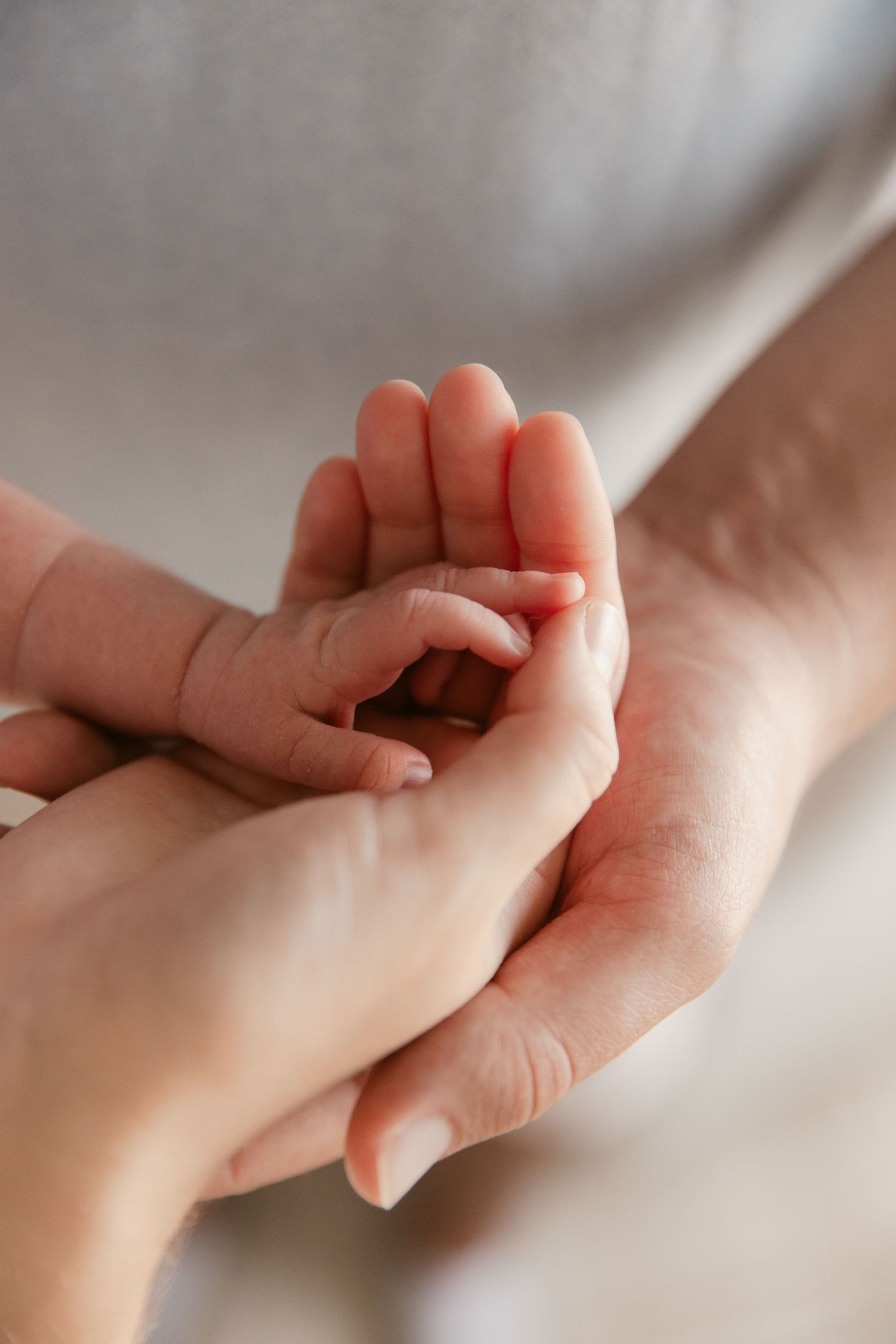 Close-up of a tiny baby hand gently holding an adult's finger against a soft white backdrop.