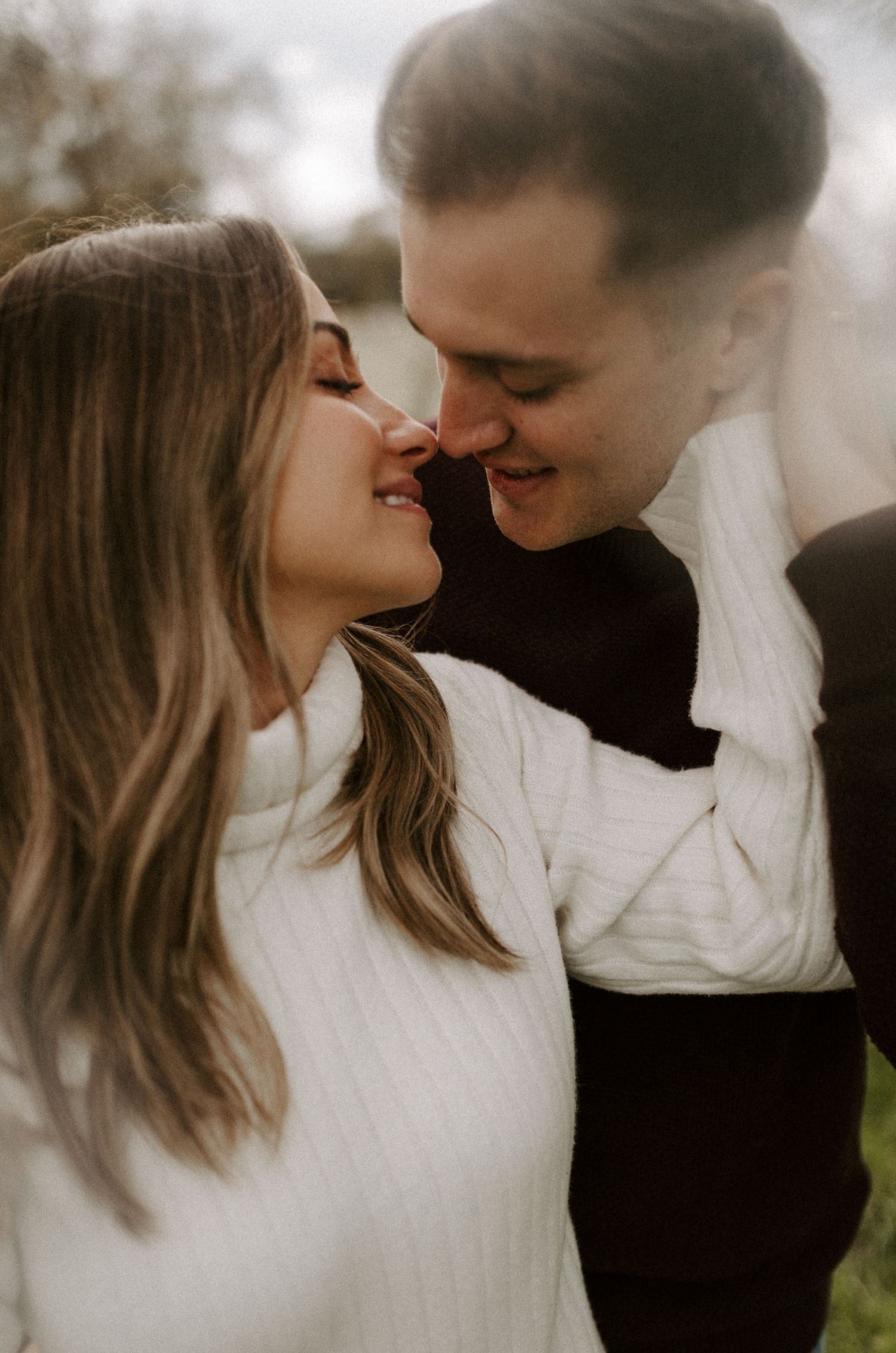 Close-up portrait of couple in white and black sweaters sharing a tender moment.