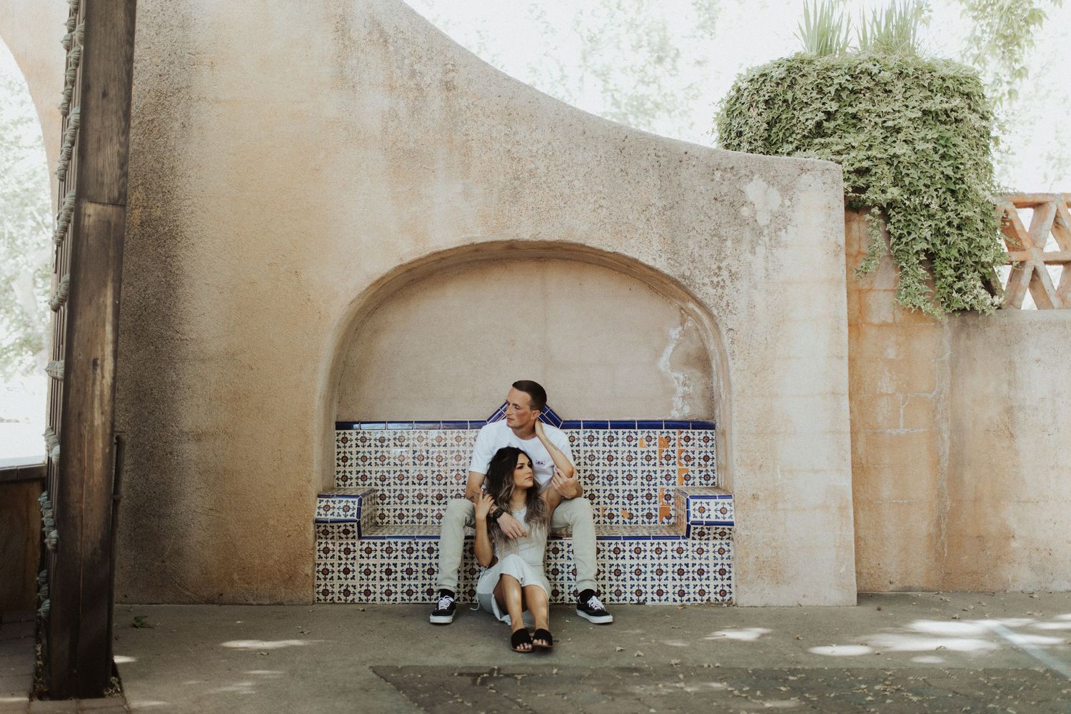 Couple sitting on tiled bench against curved architectural wall.