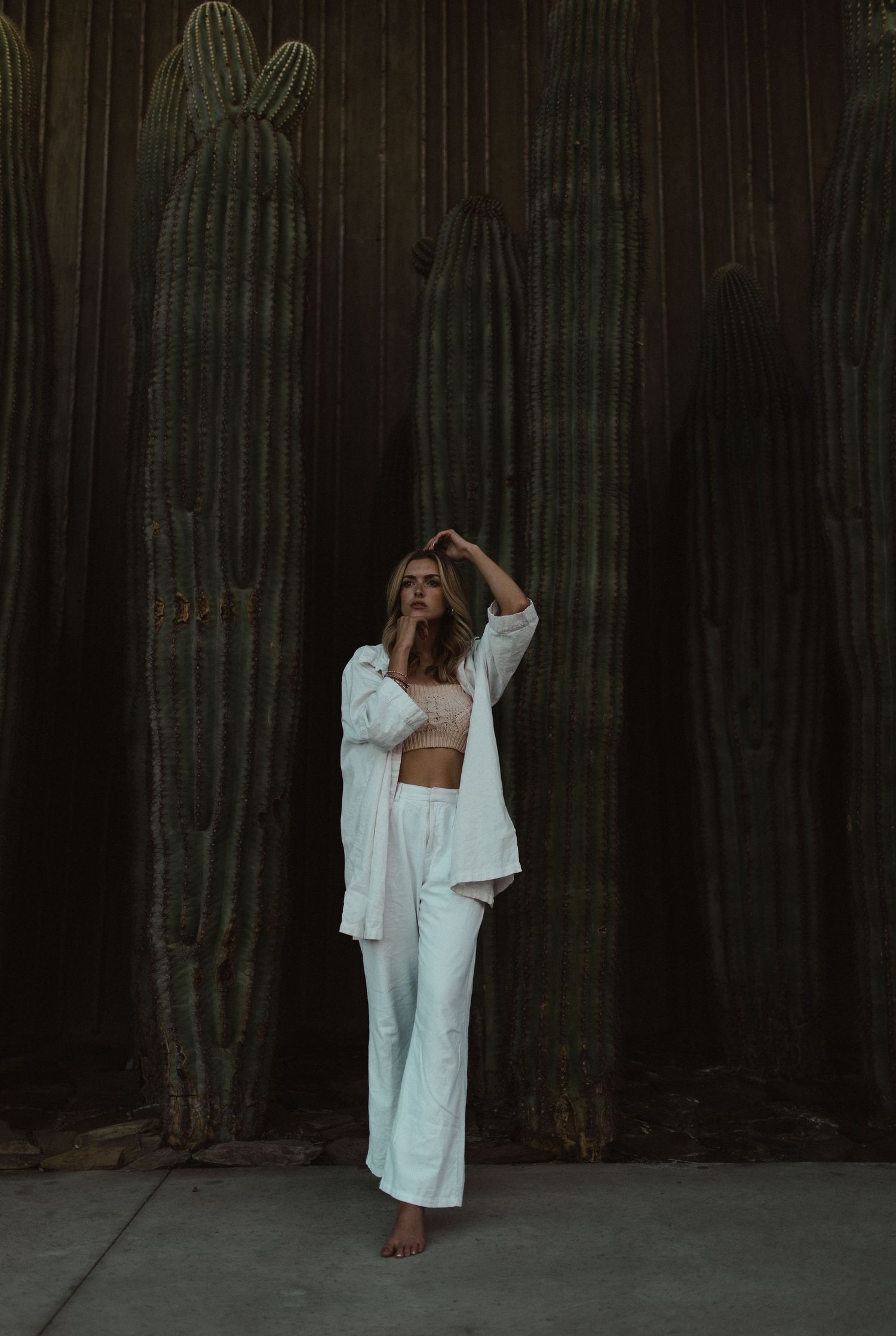 Woman in white outfit poses artistically against tall saguaro cacti.