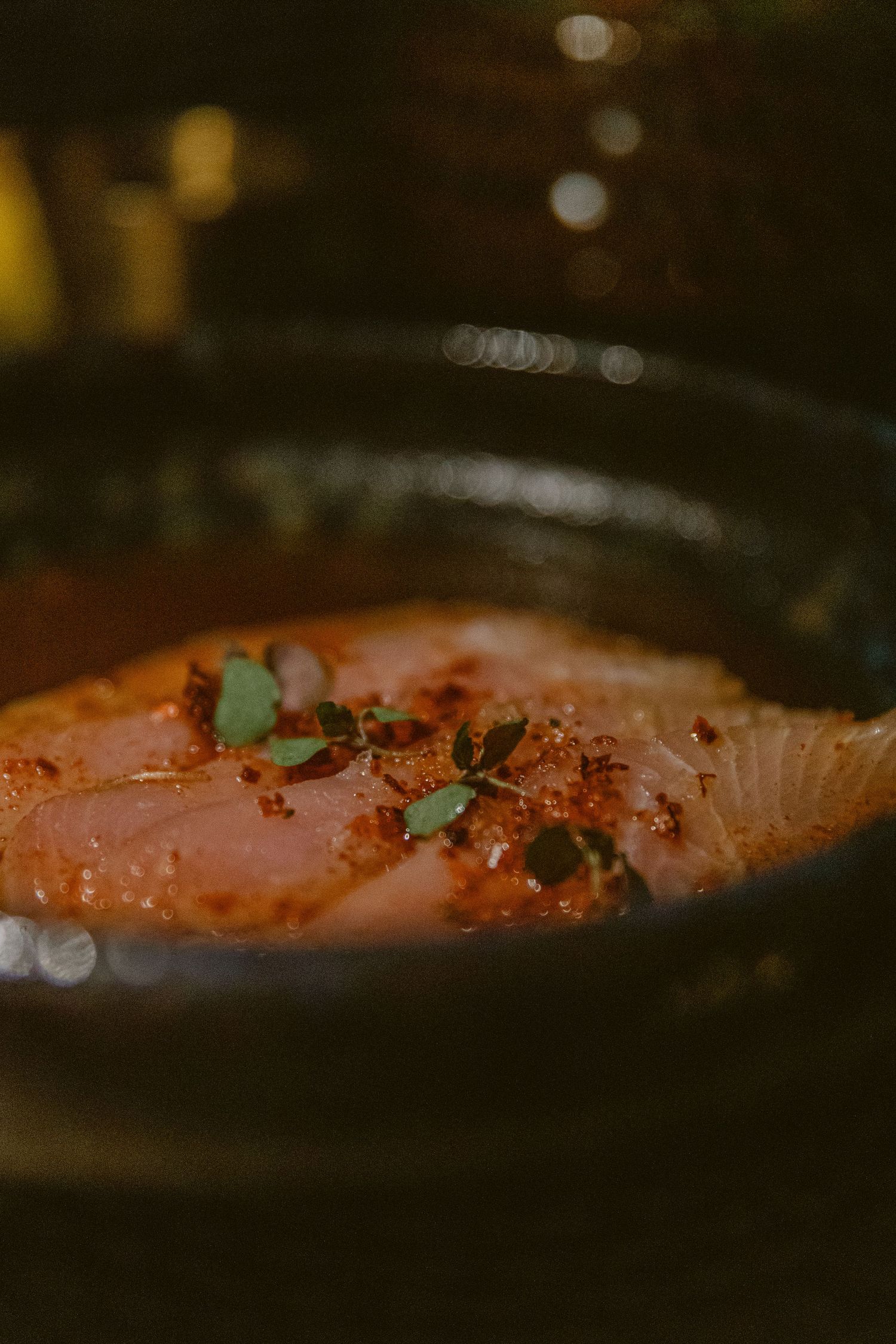Closeup of salmon fillet with herbs and spices cooking in dark lighting.