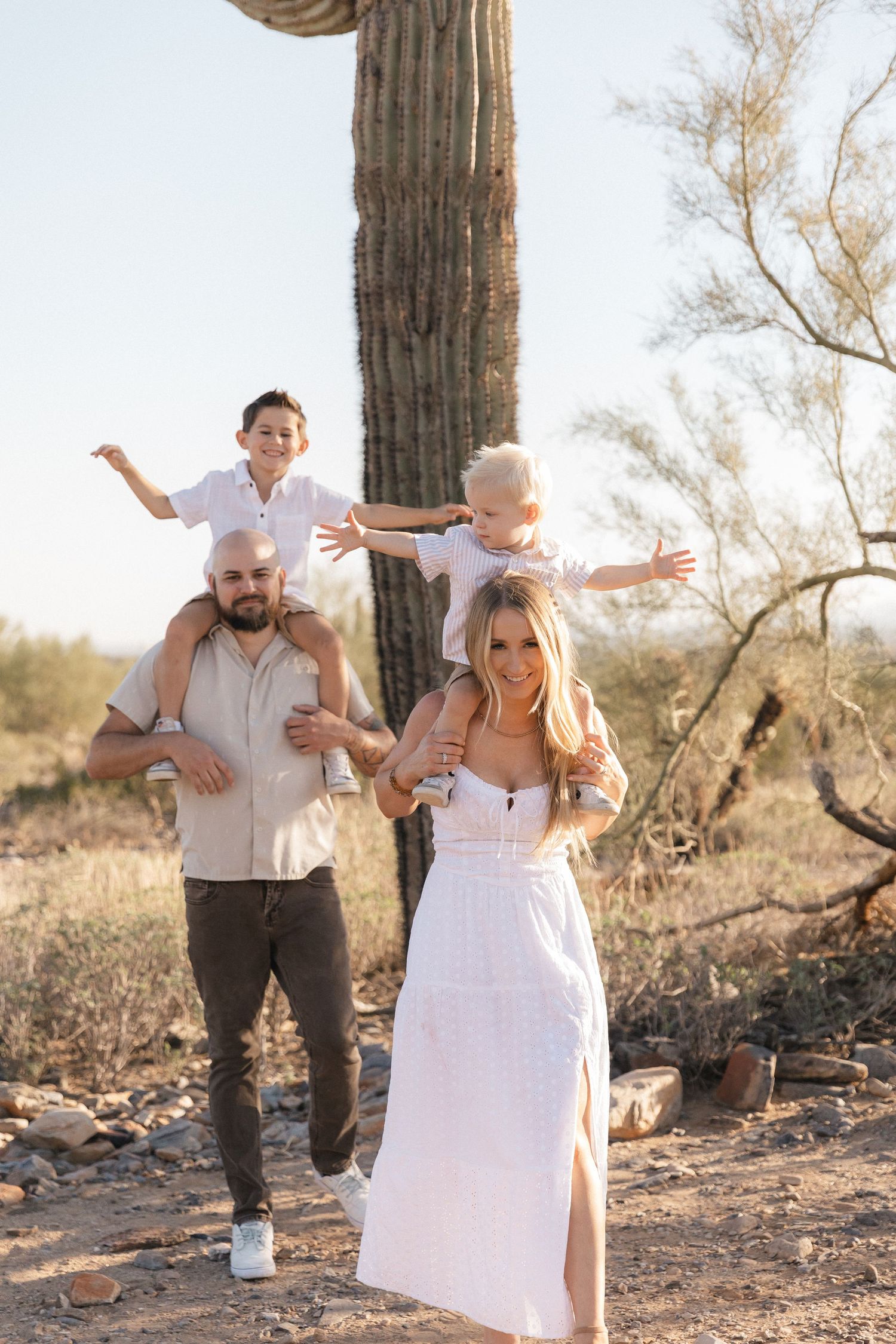 A couple shares a joyful dance moment together in a desert setting surrounded by tall saguaro cacti at sunset.