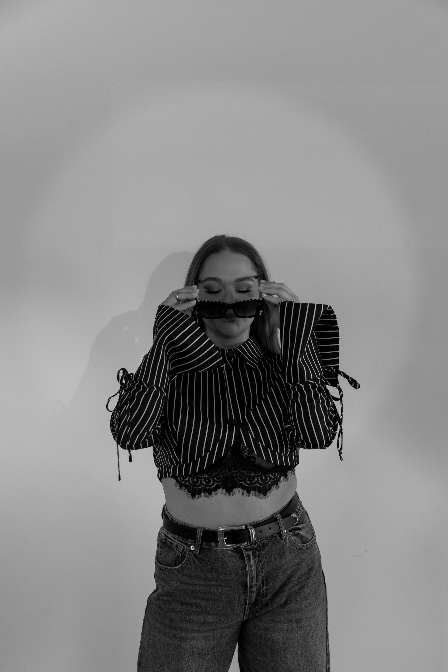 Black and white portrait of someone in a striped crop top and jeans posing against a plain background.