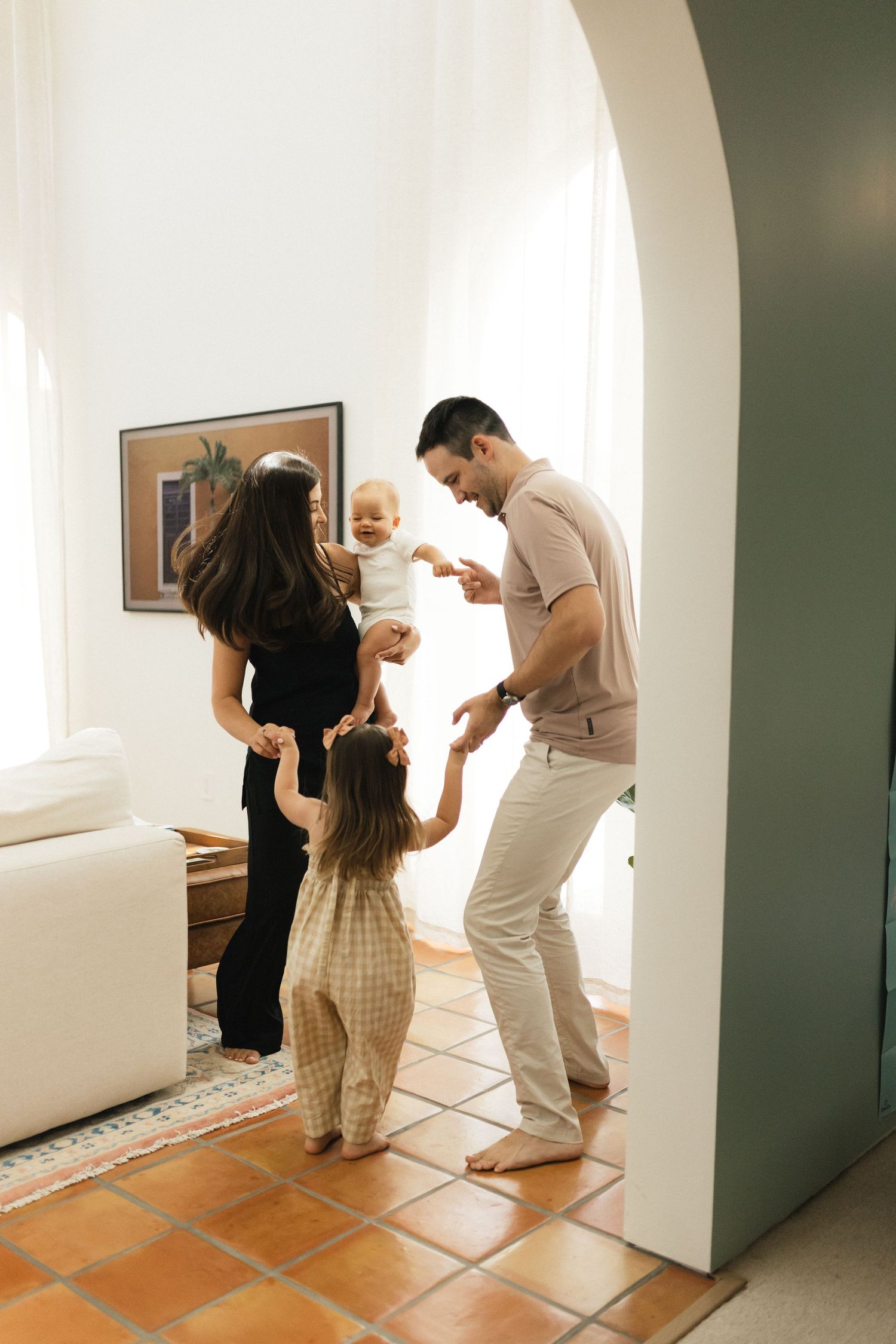 A happy family with two young children playing and dancing together in a bright modern living room with terracotta tile floors.
