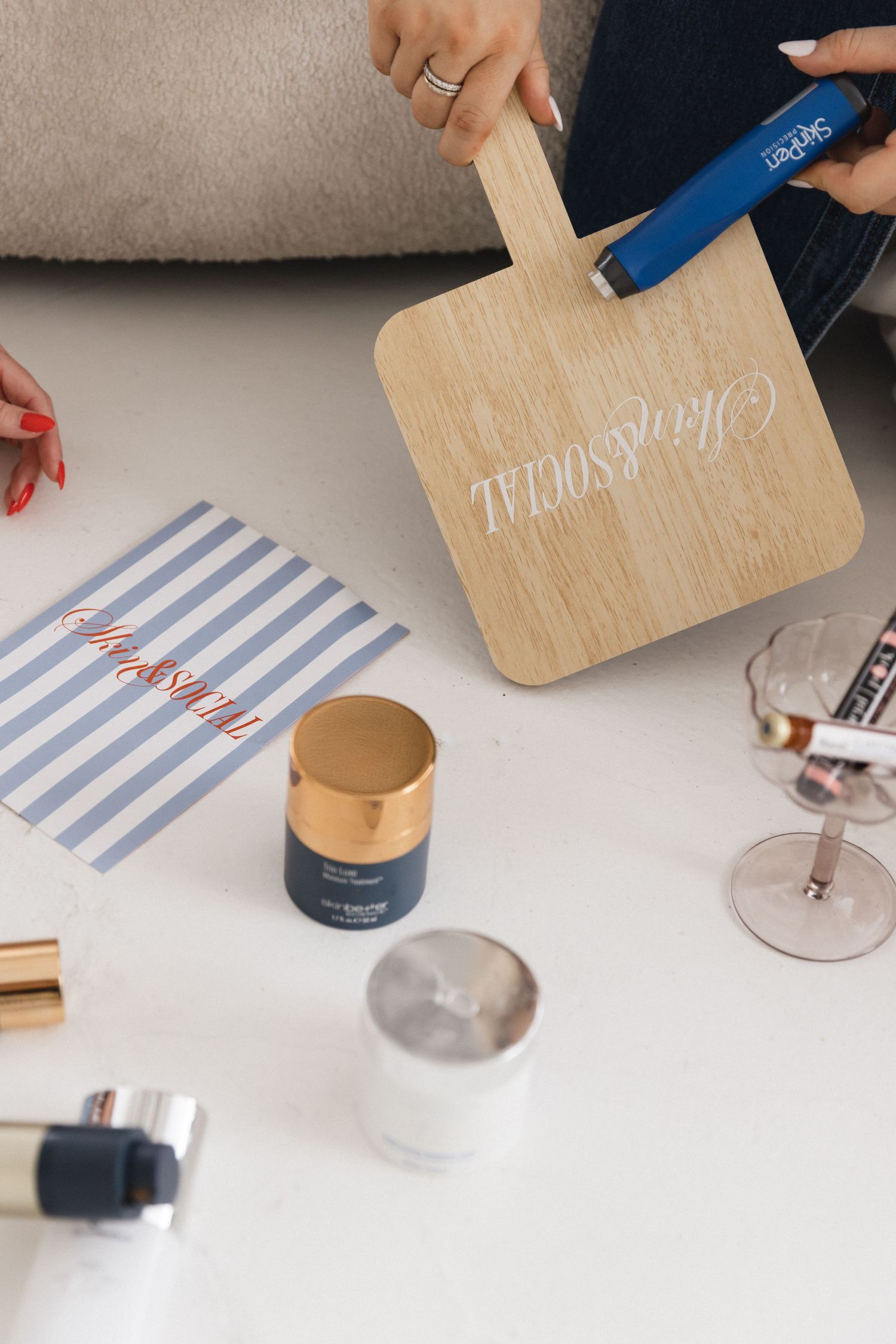 Woman holding a wooden cutting board with calligraphy, surrounded by craft supplies and a striped card on white surface.