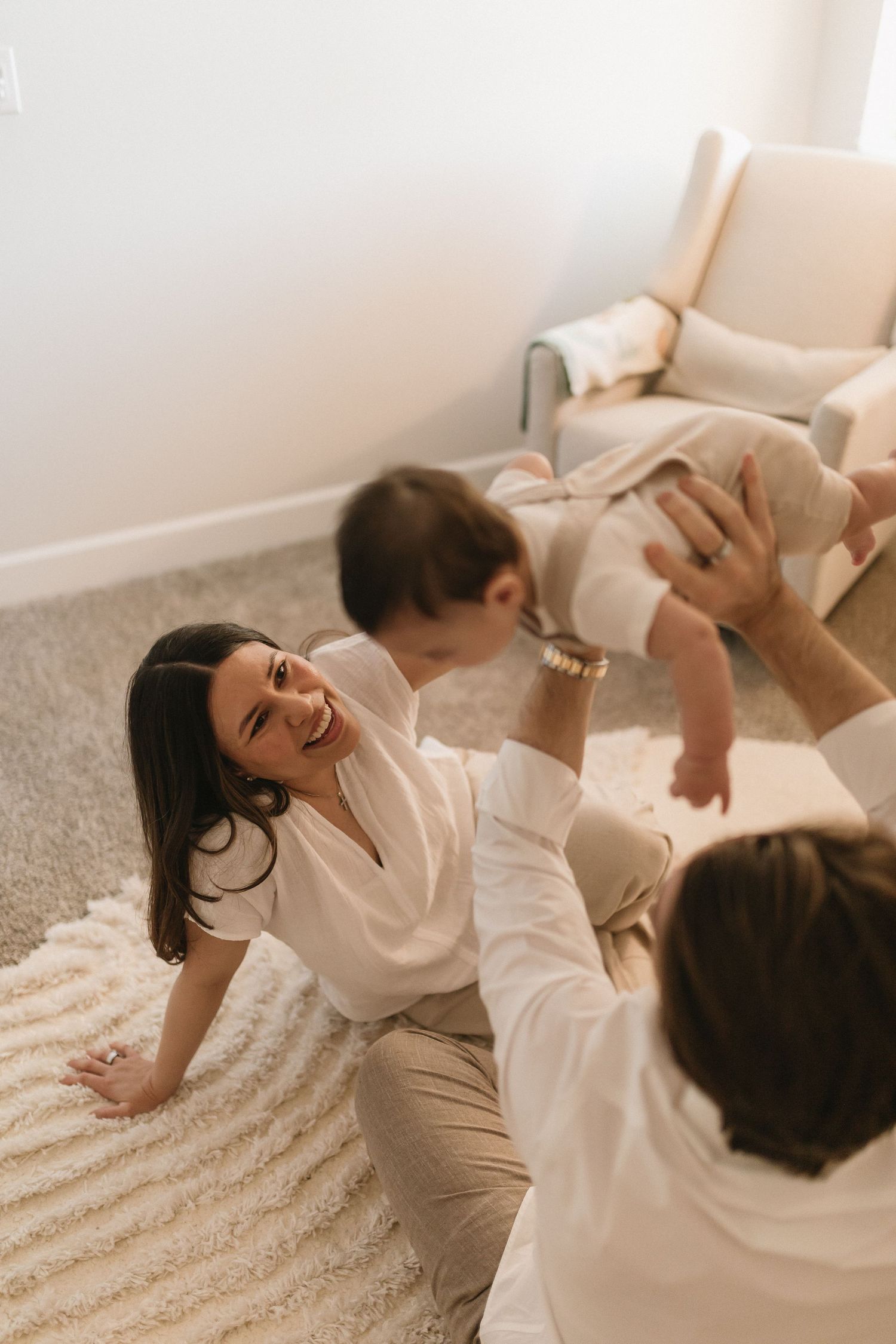 Two people in white outfits share joyful moments together on a light-colored carpet in a bright room.