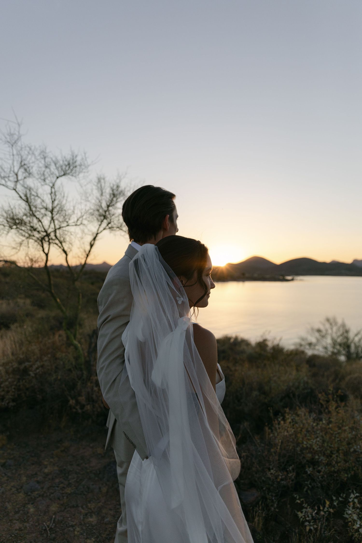 A silhouetted couple embraces while watching the sunset over a mountain lake.