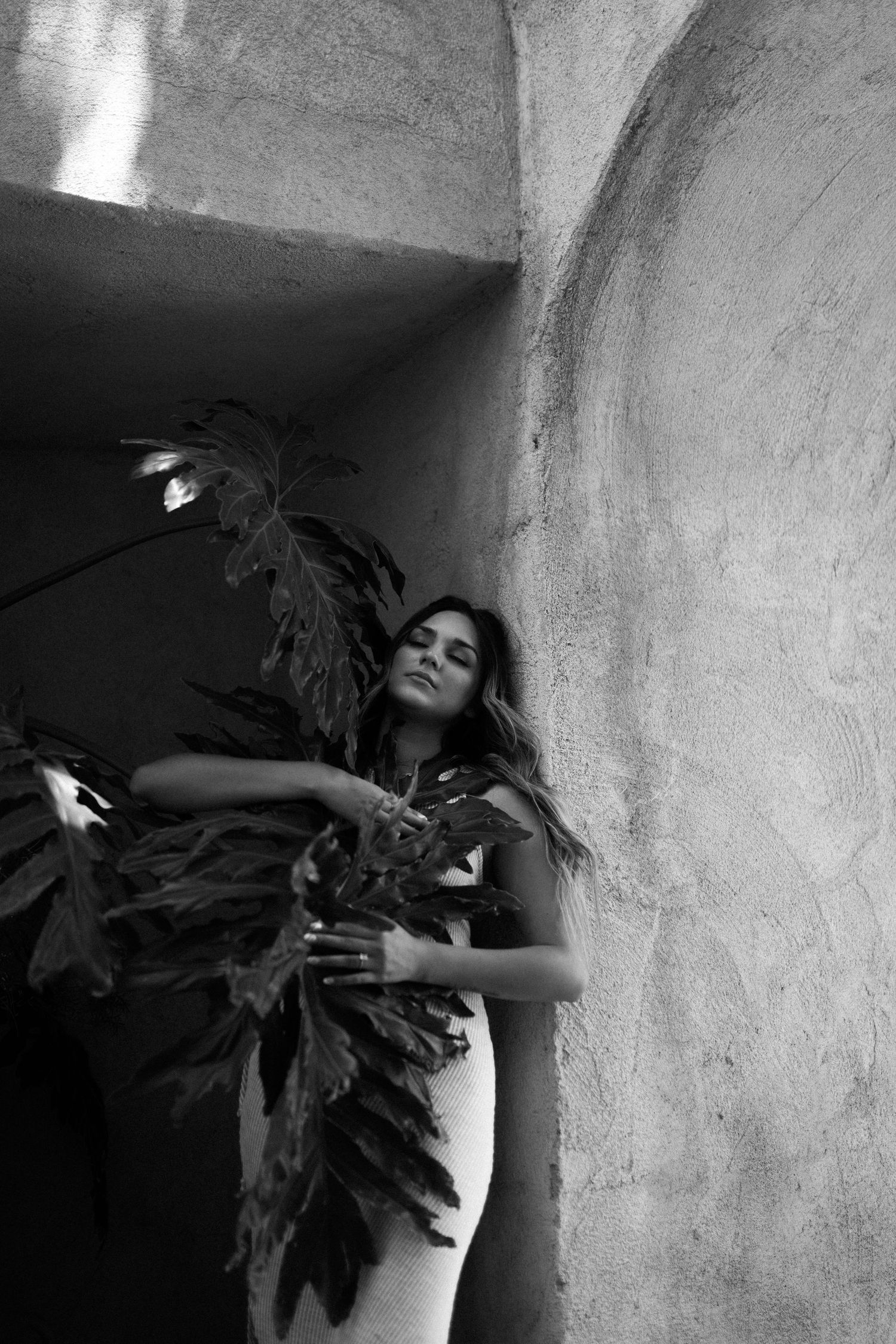 Artistic black and white portrait of person with tropical leaves in shadowed archway.