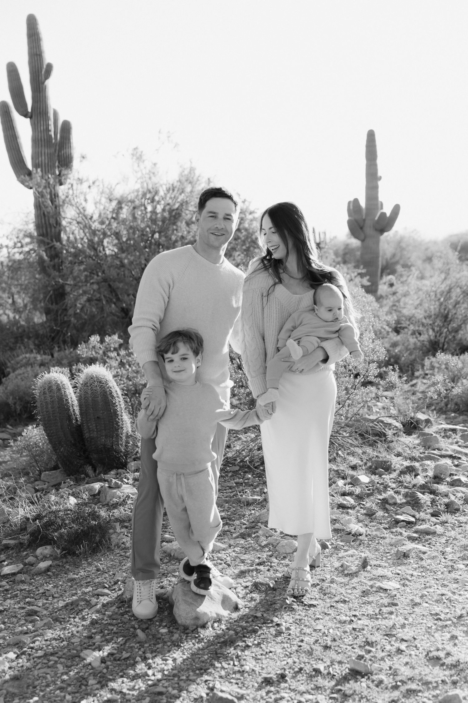 Family poses together in desert landscape with tall saguaro cactus against bright sky.
