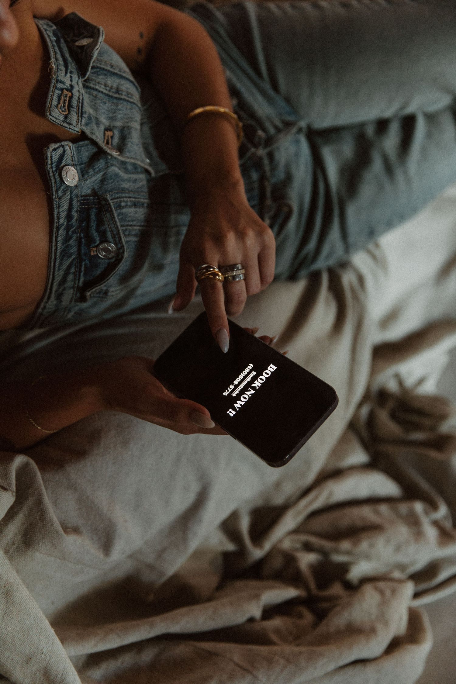 Person in denim holding a smartphone while relaxing on comfortable seating.
