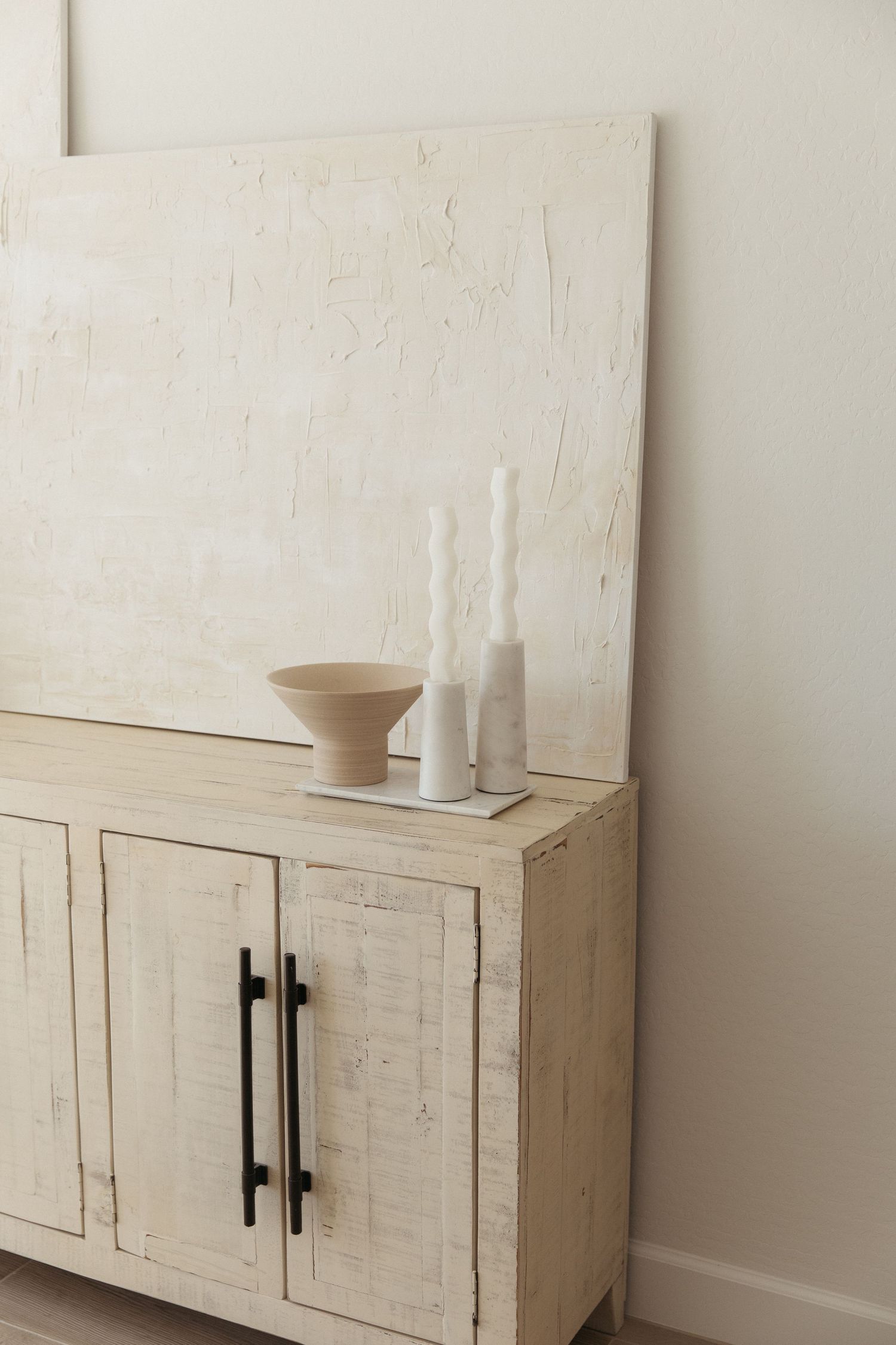 Rustic white cabinet with decorative vases and candles against neutral wall in minimalist style.