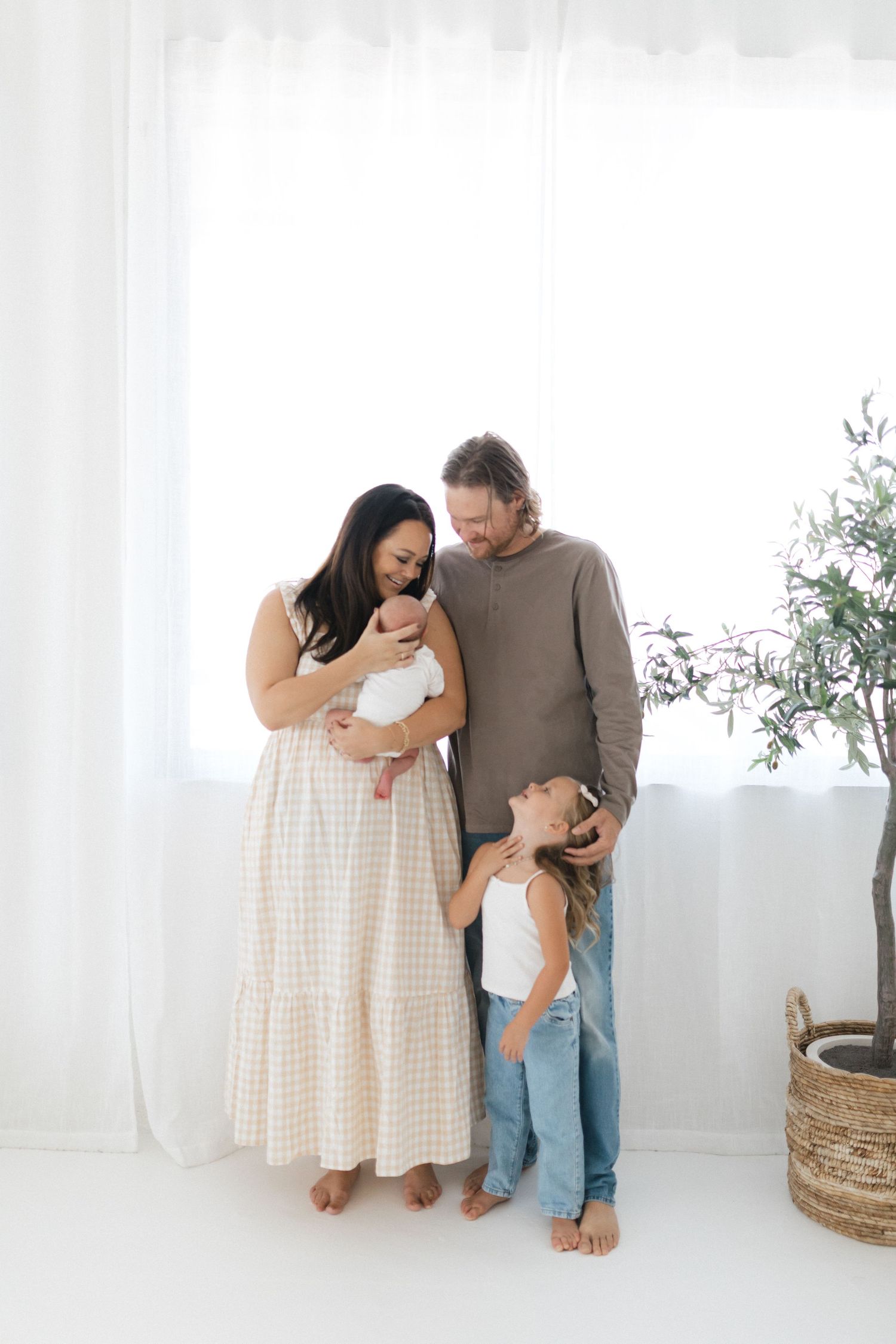 A family shares tender moments together in a bright white studio setting with minimalist decor.