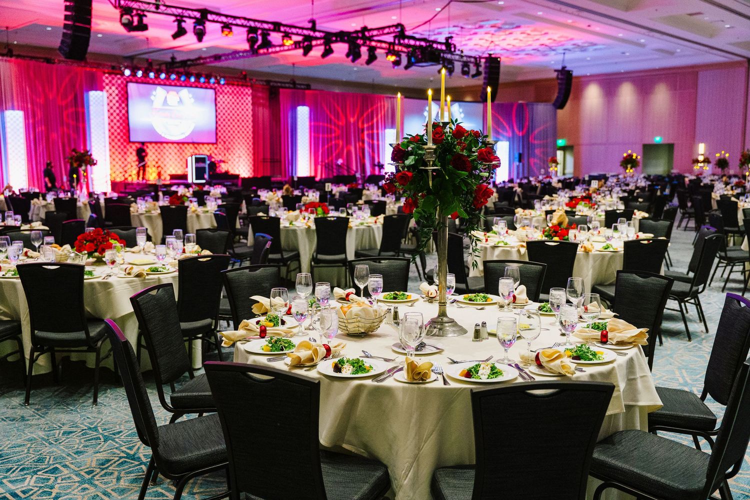 Elegant banquet hall setup with round tables, floral centerpieces and dramatic red lighting.
