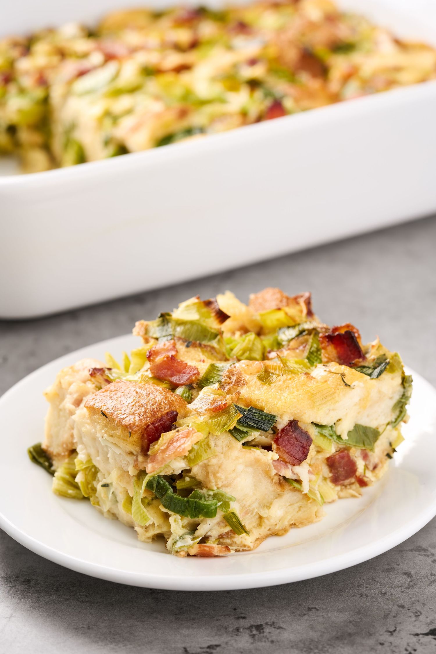 Chicken Brussels sprouts casserole with bacon and melted cheese served on white plate and baking dish.