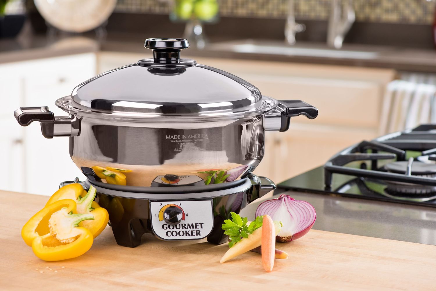 Stainless steel electric skillet on kitchen counter with fresh vegetables and onions for cooking.