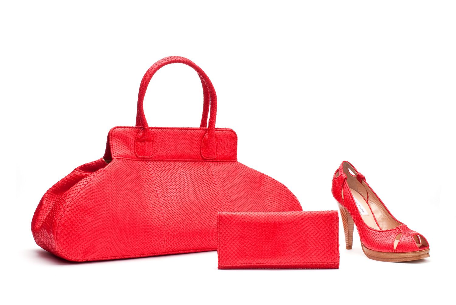 Red fashion accessories including a handbag, wallet and peep-toe high heel shoe arranged on white background.