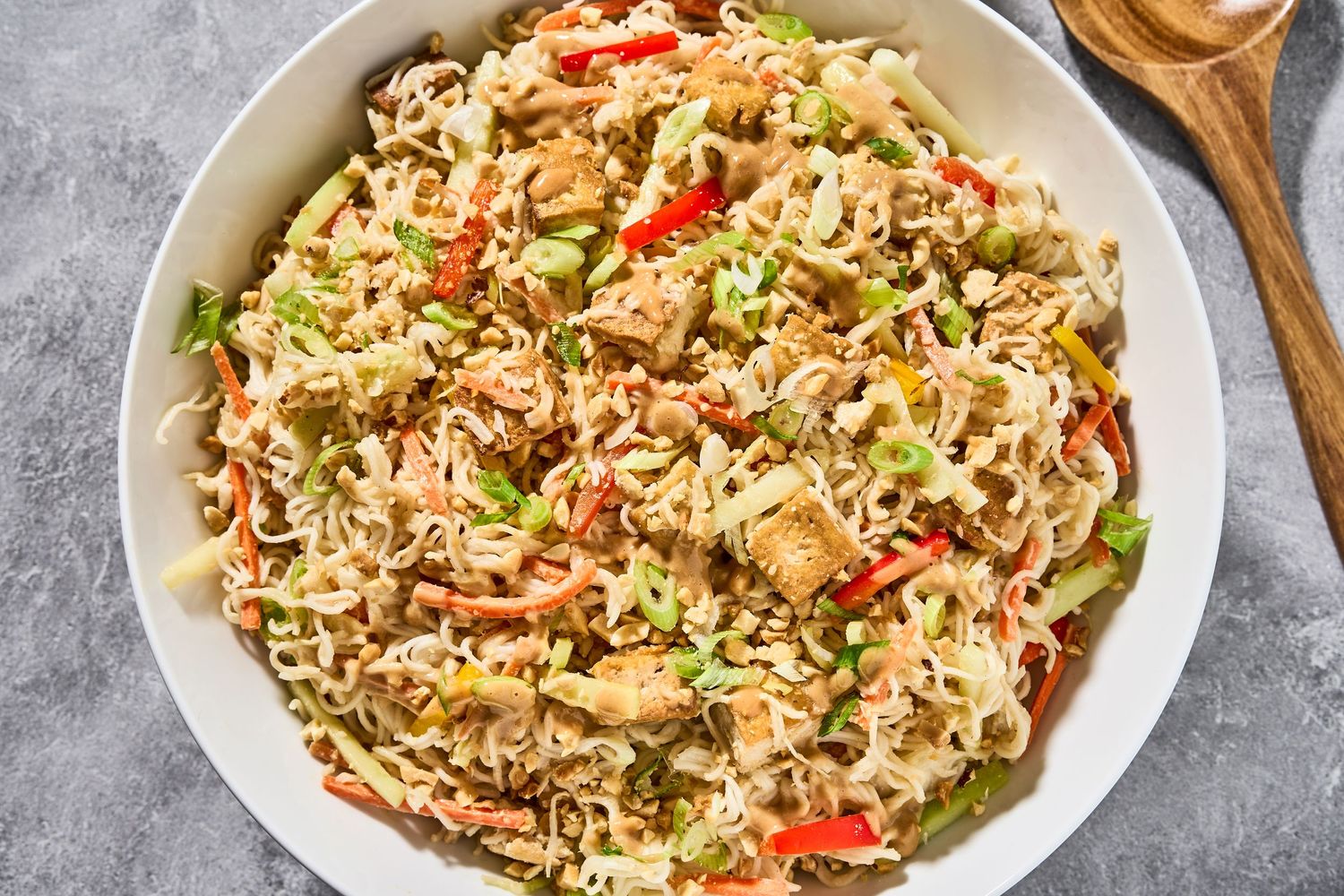 A white bowl filled with homemade chicken fried rice garnished with green onions and red peppers on a gray surface.