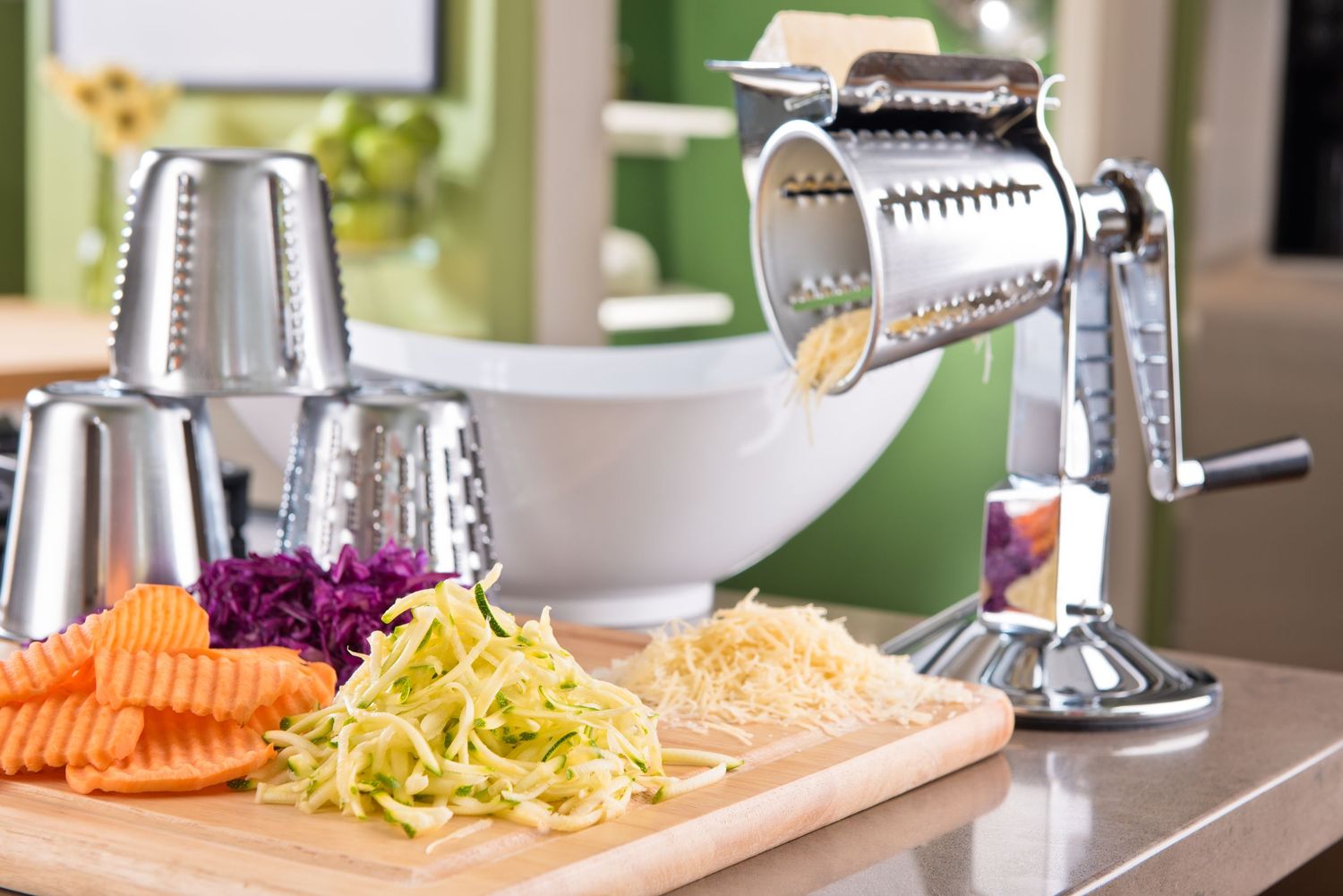 Carrots and yellow zucchini being spiralized into thin noodles on a kitchen counter with stainless steel appliances.