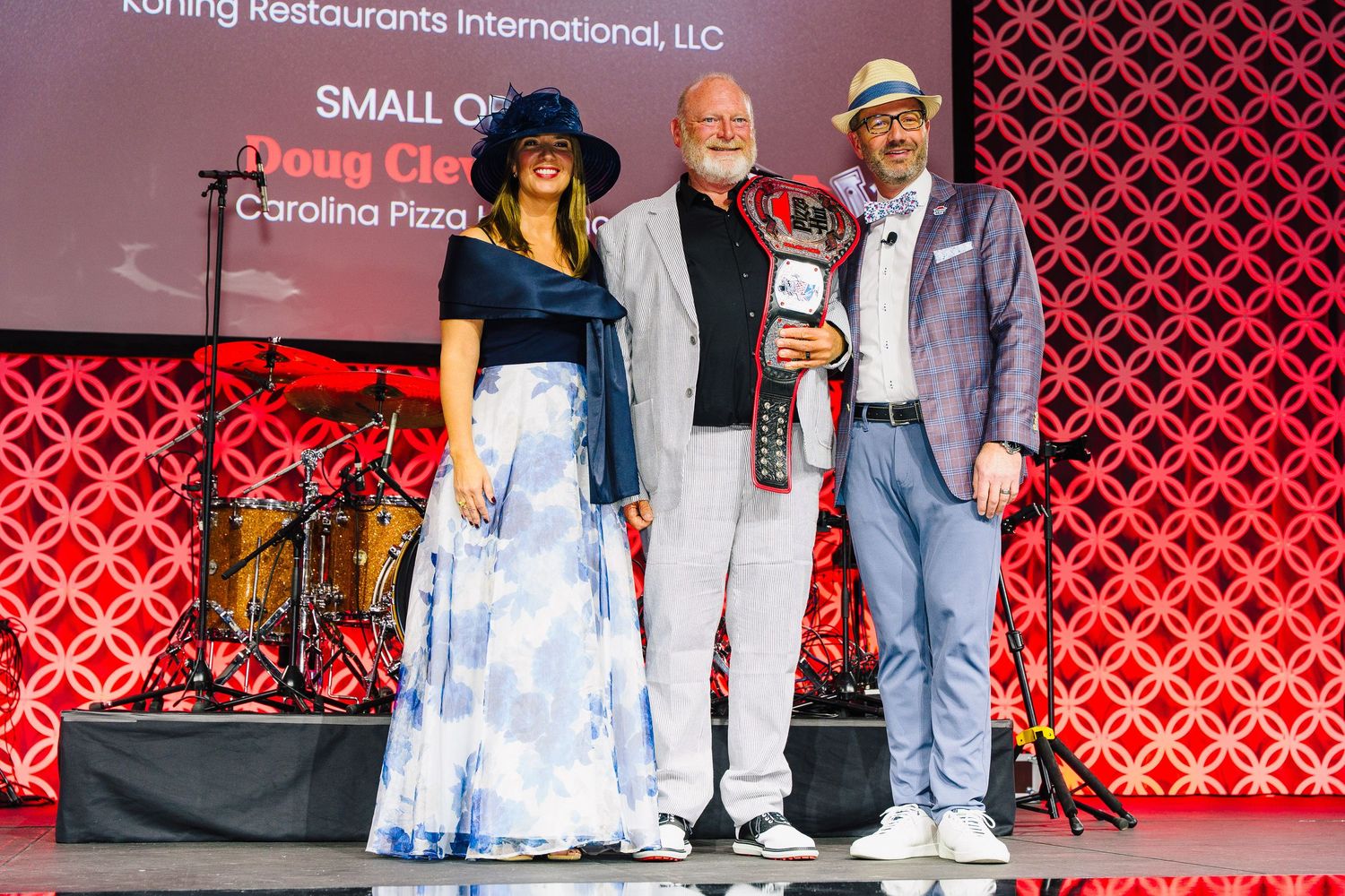 Award ceremony on stage with red geometric backdrop and western-themed attire.