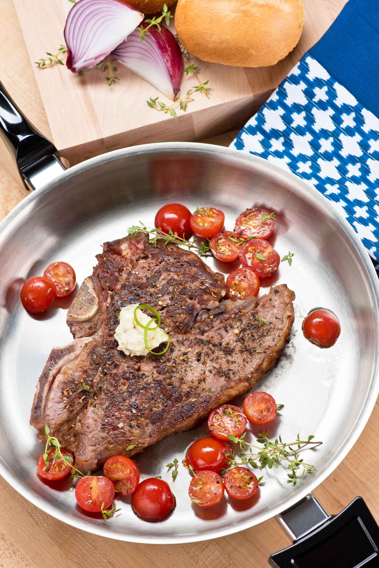 Three grilled steaks on white ceramic plates with cherry tomatoes and fresh herbs arranged side by side.
