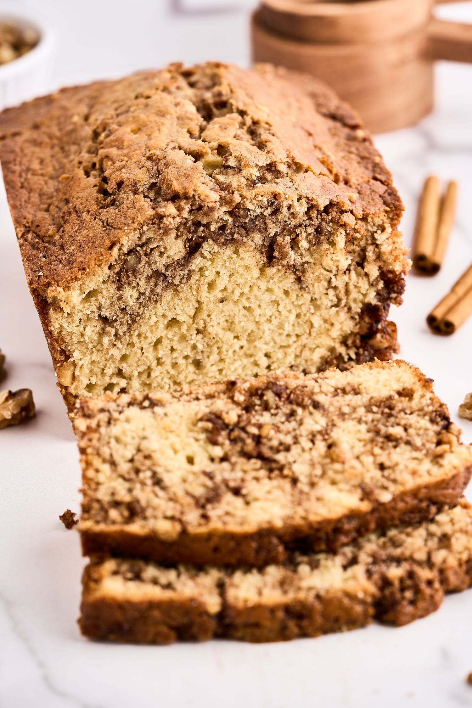 A sliced cinnamon swirl quick bread loaf with a marbled pattern and cinnamon sticks on a white marble surface.