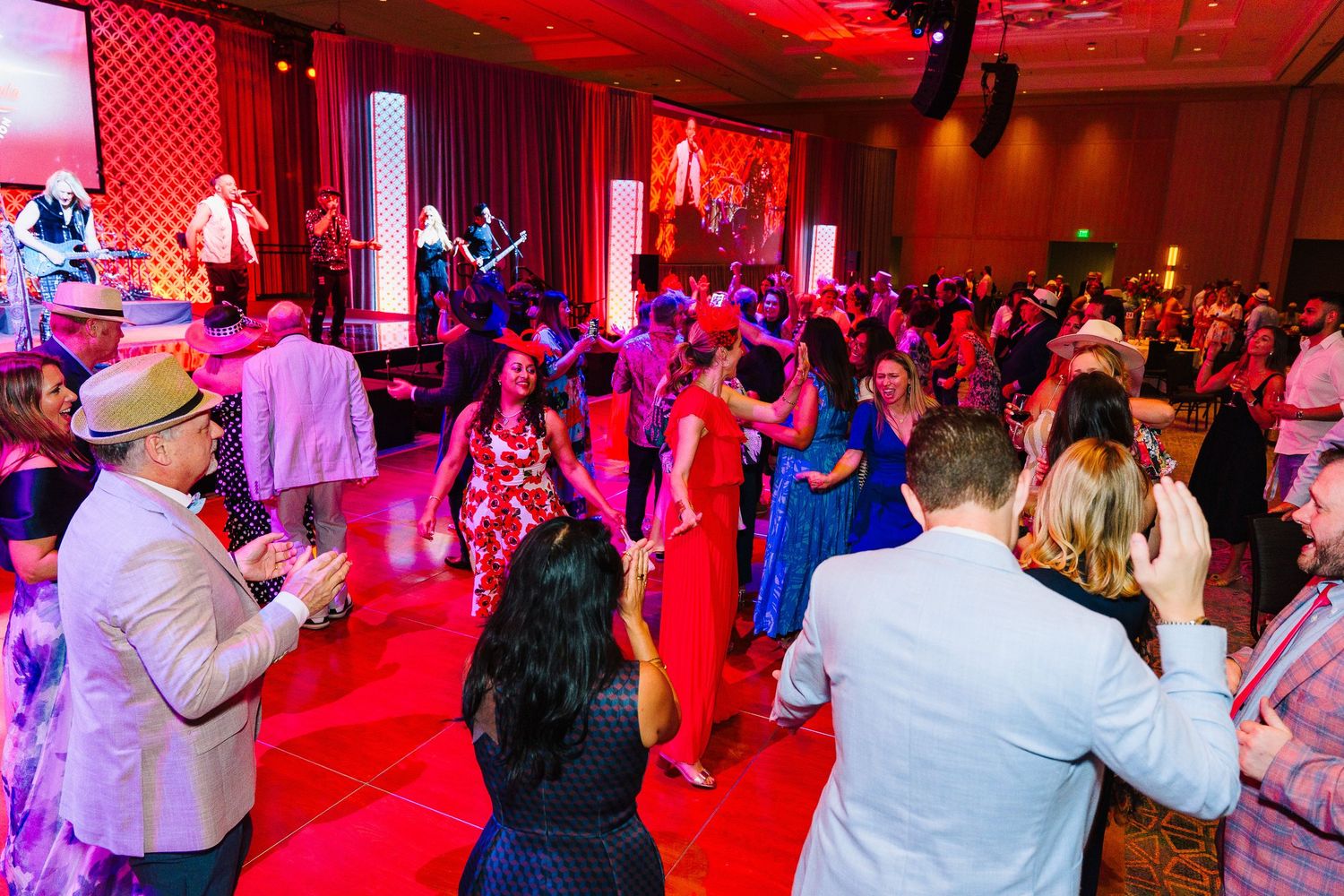 Crowd dancing at an event with red ambient lighting and live band performing.