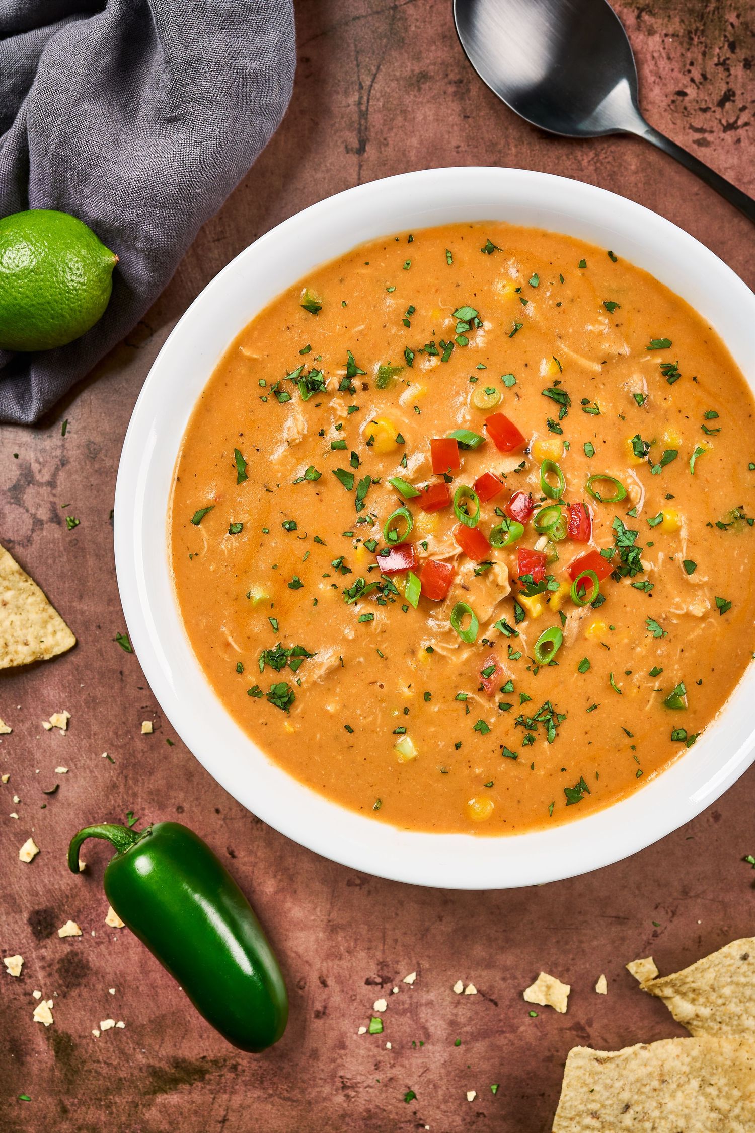 Creamy queso dip in white bowls garnished with red peppers, jalapenos and fresh herbs, served with tortilla chips.