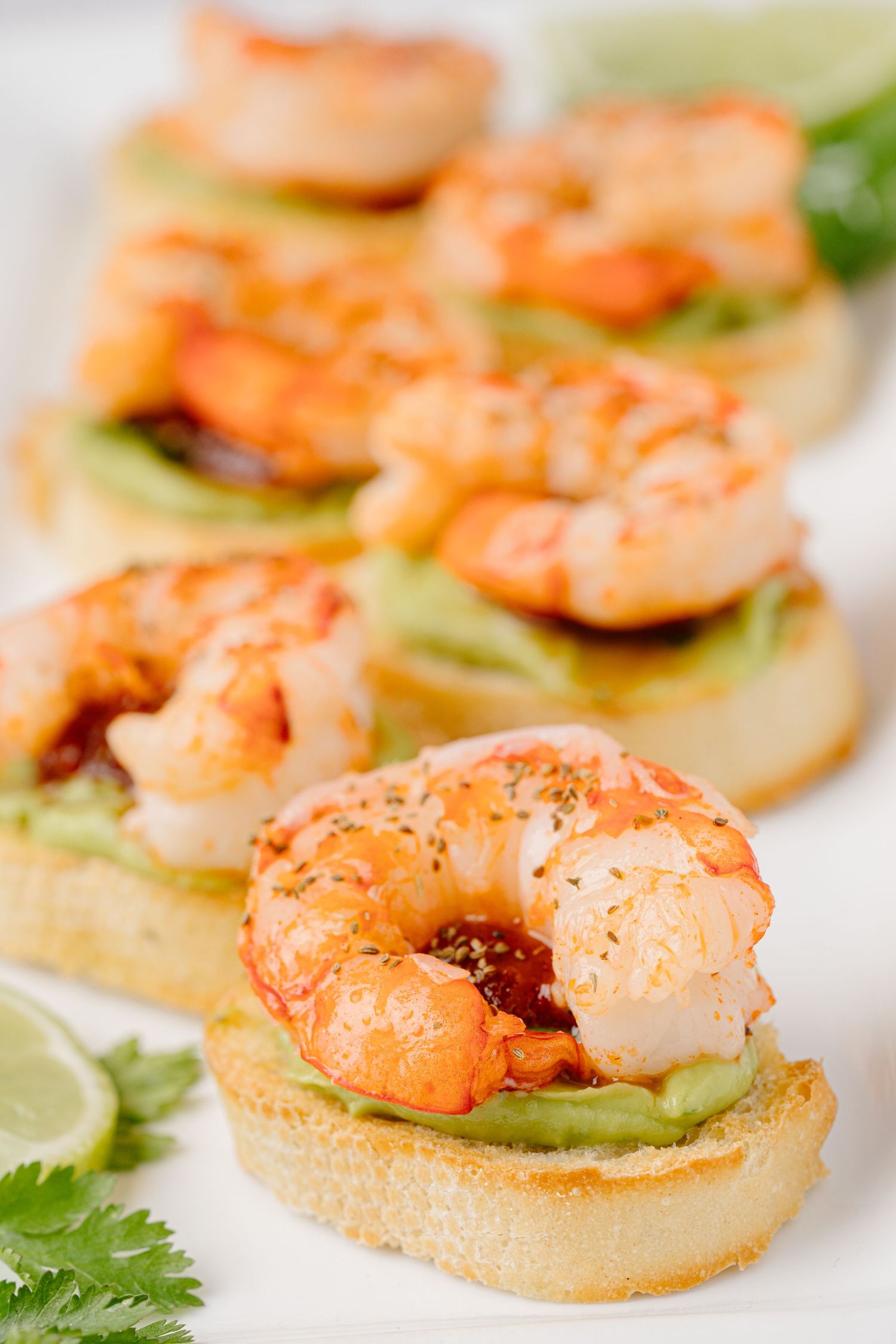 Grilled shrimp crostini appetizers with avocado spread and lime garnish served on toasted baguette slices.
