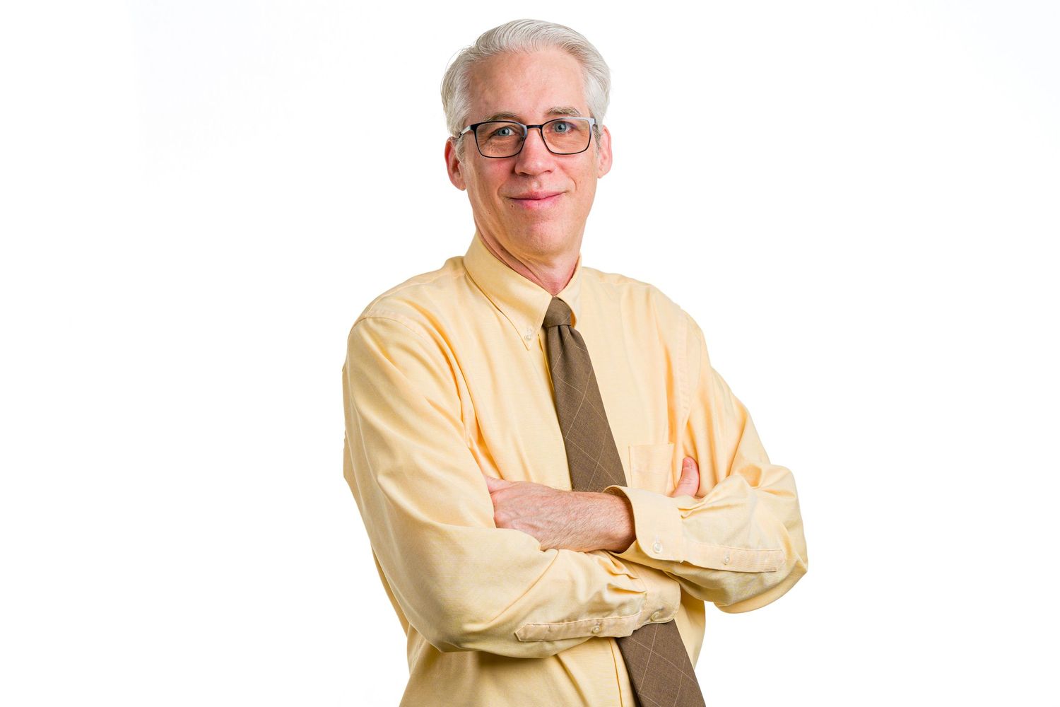 Professional wearing a yellow dress shirt and tie poses with crossed arms.