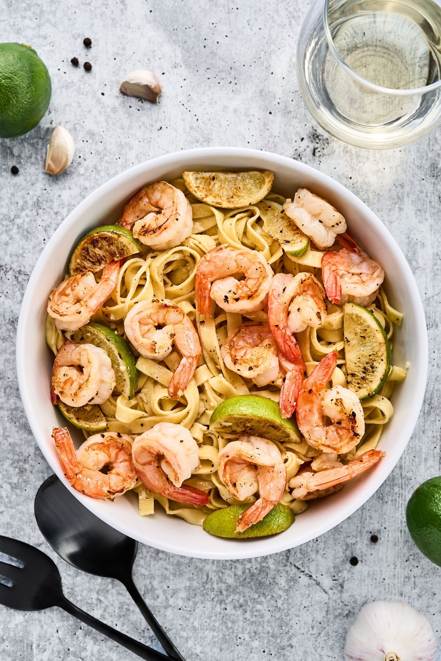 Shrimp scampi pasta with white wine sauce, garlic and lime served in a white bowl on light gray background.