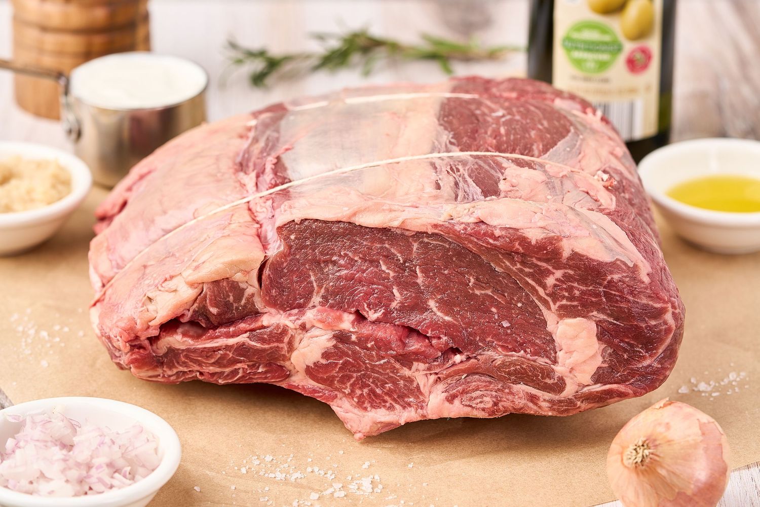 Raw beef ribeye steaks arranged on a butcher block with spices and ingredients for cooking.