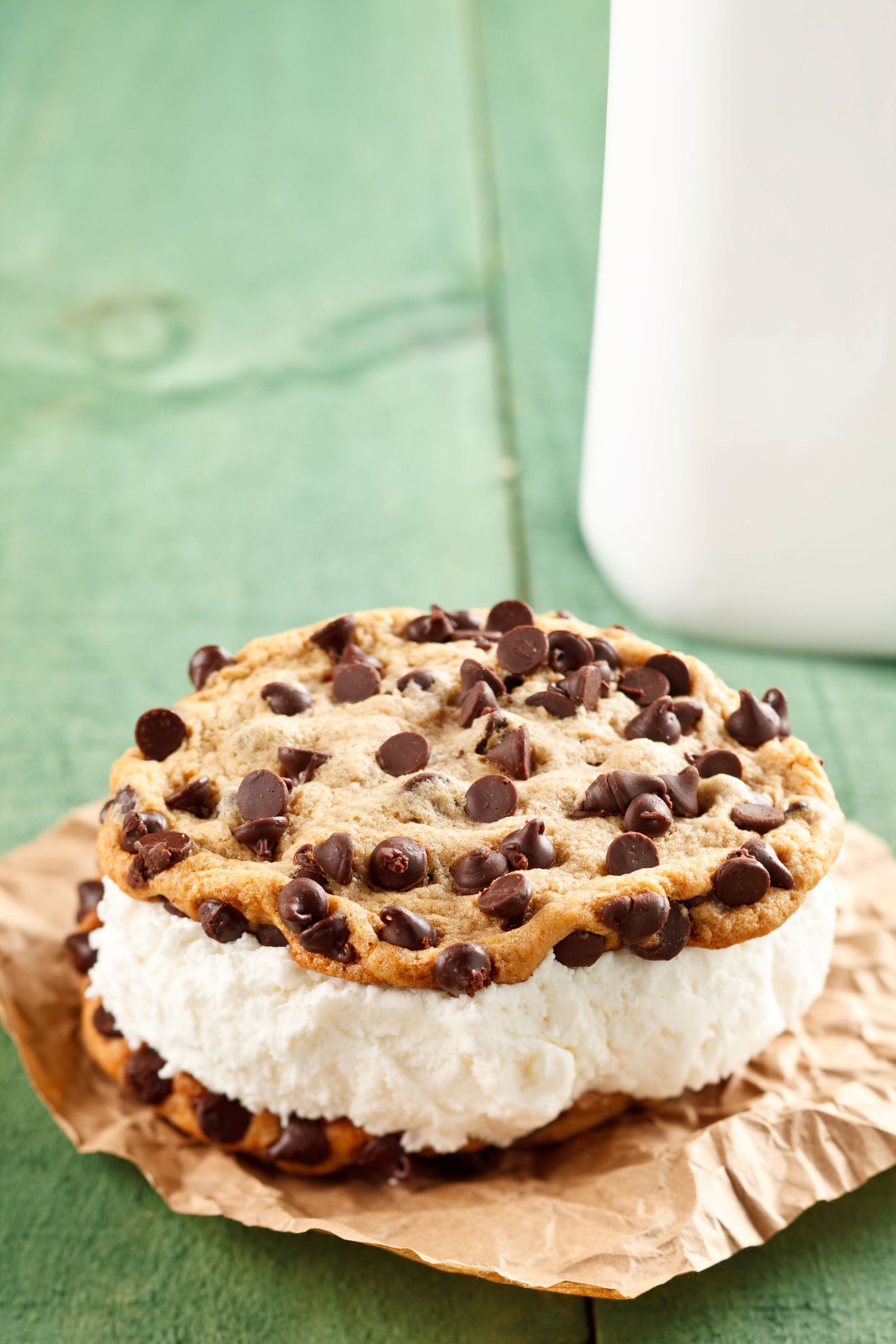 Cookie dough ice cream sandwich topped with chocolate chips on brown parchment paper.