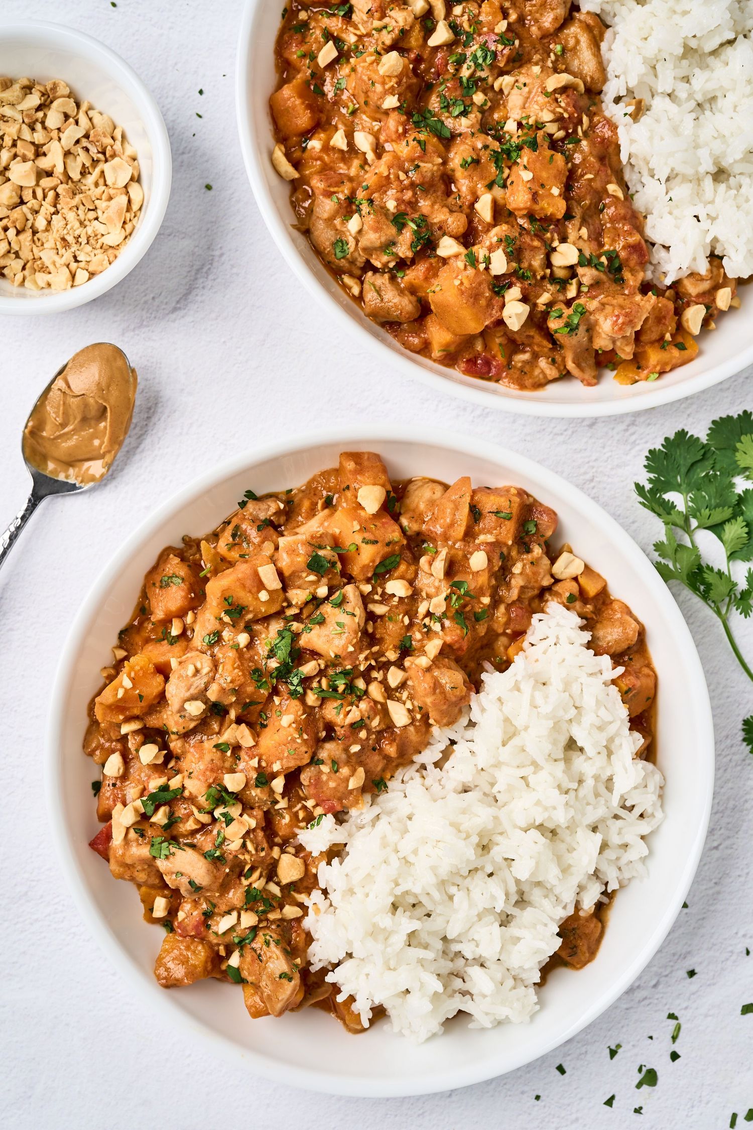 Creamy chicken casserole with white rice, garnished with chopped peanuts and fresh herbs on white plates.