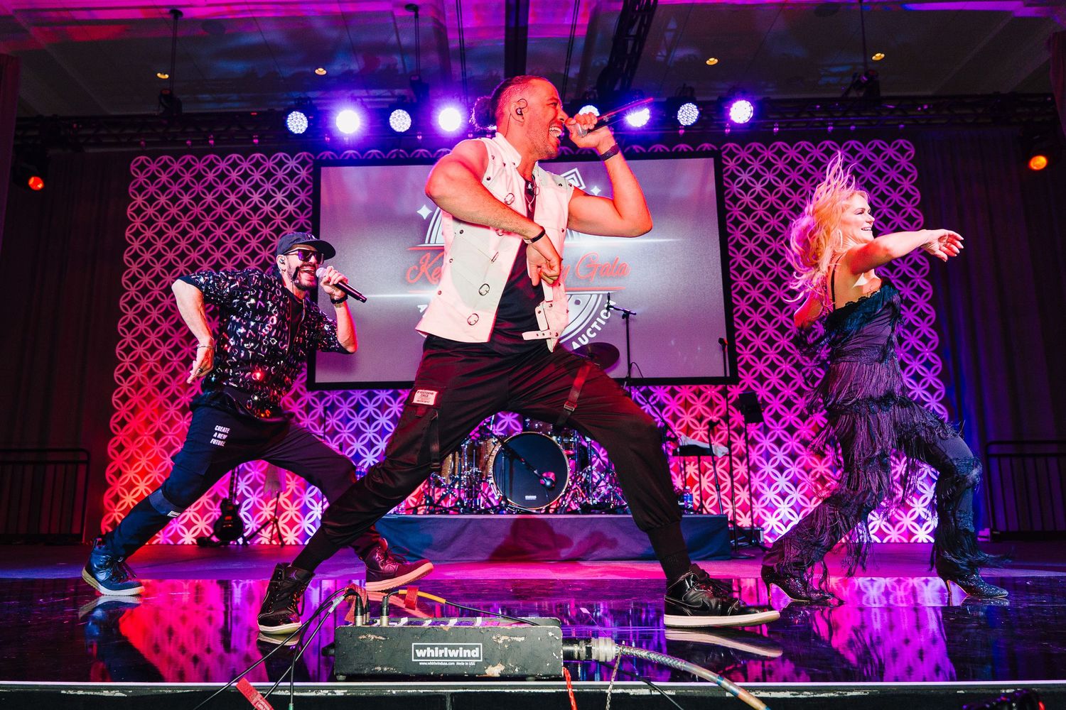 Dynamic stage performance with dancers silhouetted against vibrant purple and red lighting.