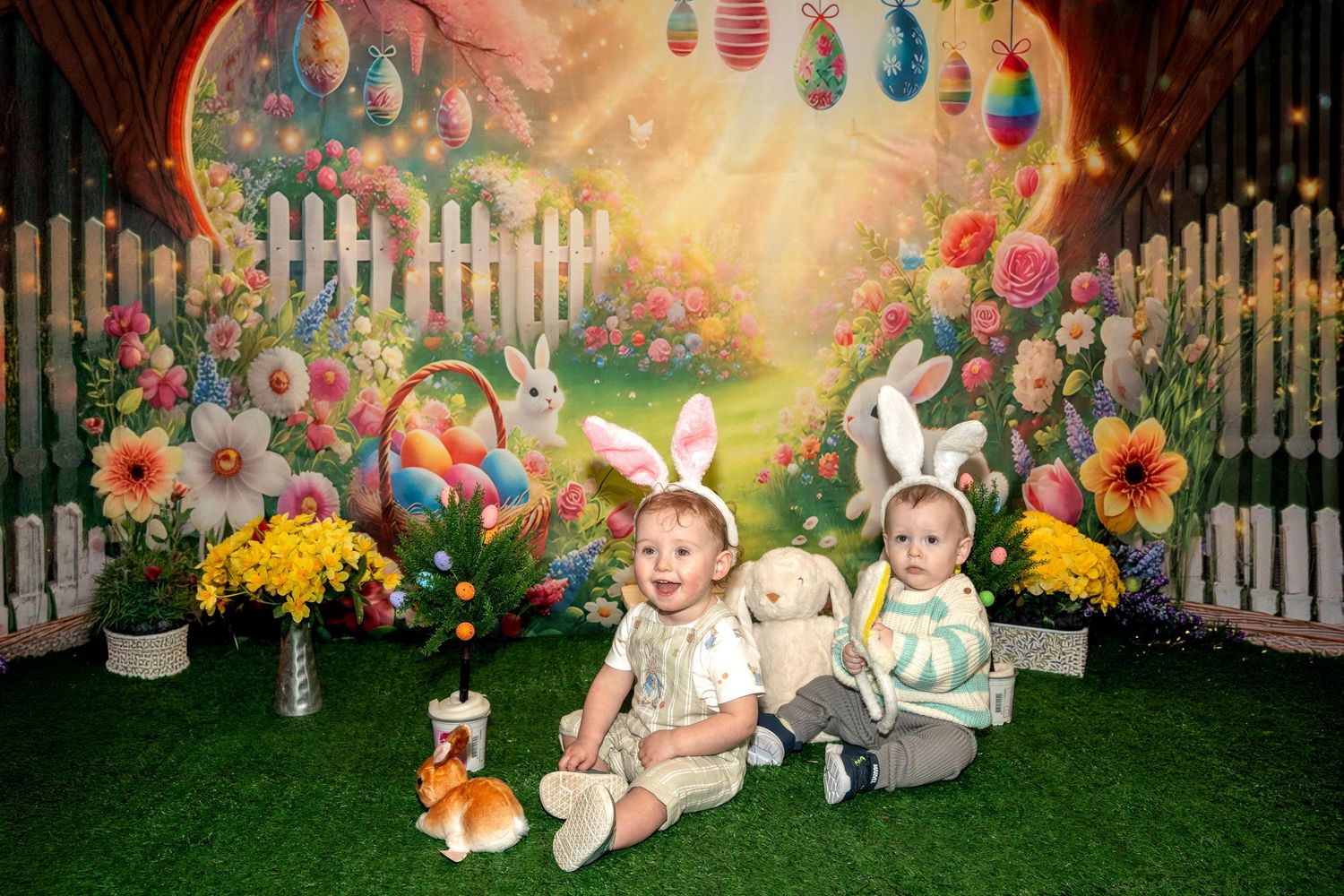 Easter themed outdoor photo setup with colorful eggs, spring flowers, and white picket fence in magical garden lighting.