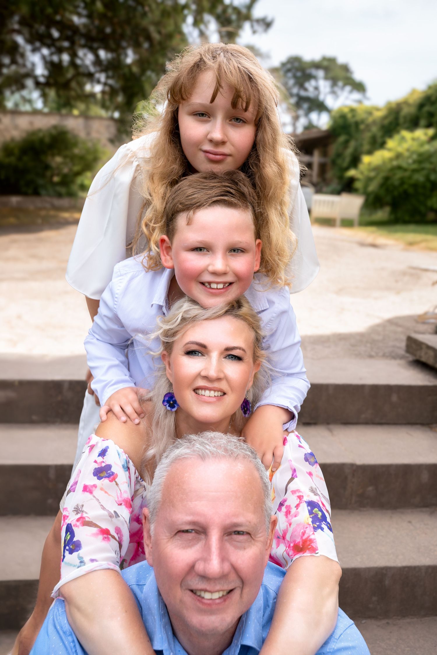 Happy family of four posing on outdoor steps, parents and two children stacked in a playful portrait.
