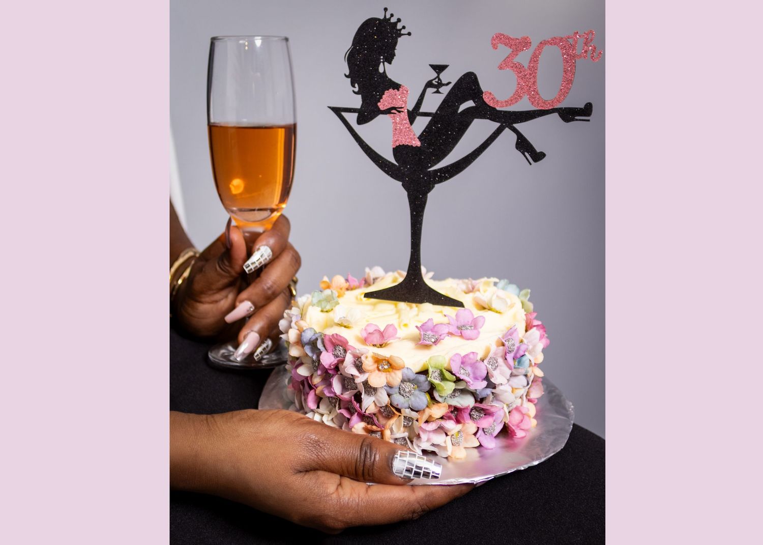 A white birthday cake decorated with pink flowers and a black silhouette cake topper, with a champagne glass toast. Birthday photo